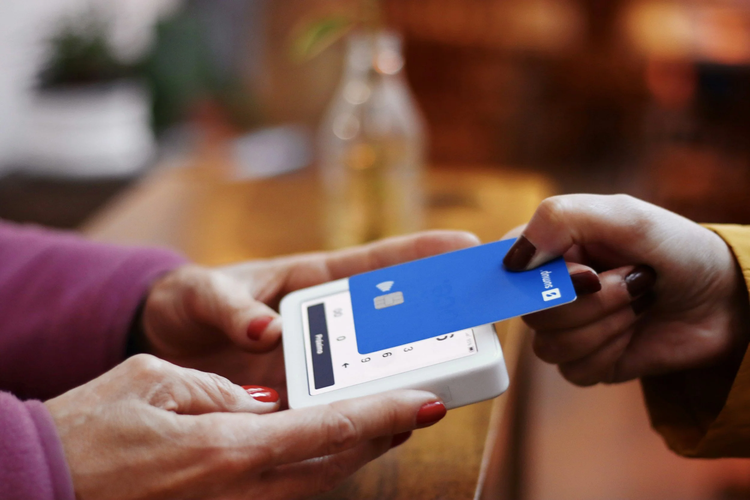 A person using a mobile device to scan a blue credit card held by another person, in a cozy indoor setting.