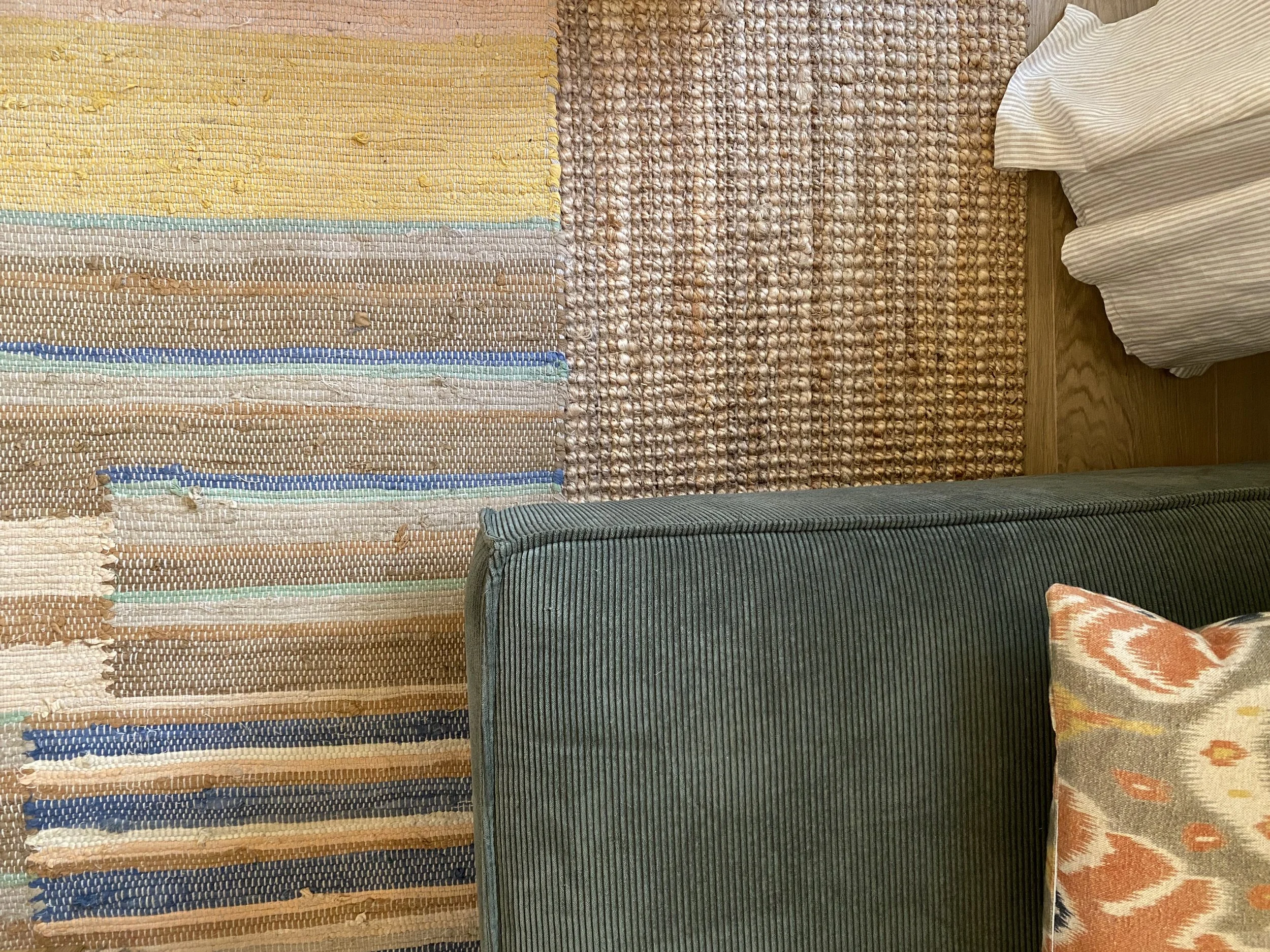 A collection of various woven rugs and a striped upholstered chair, arranged on a wooden floor, with a corner of a floral-patterned cushion visible.