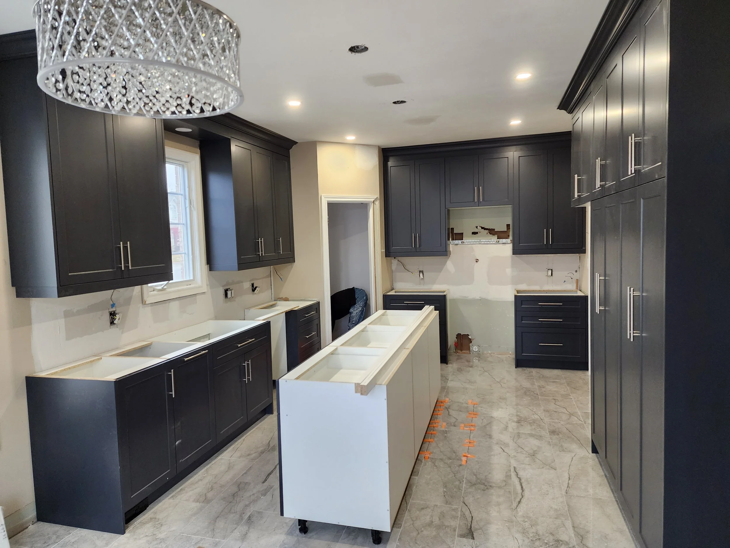 Kitchen under renovation with dark gray cabinets, an island with a white base, and appliances not yet installed.