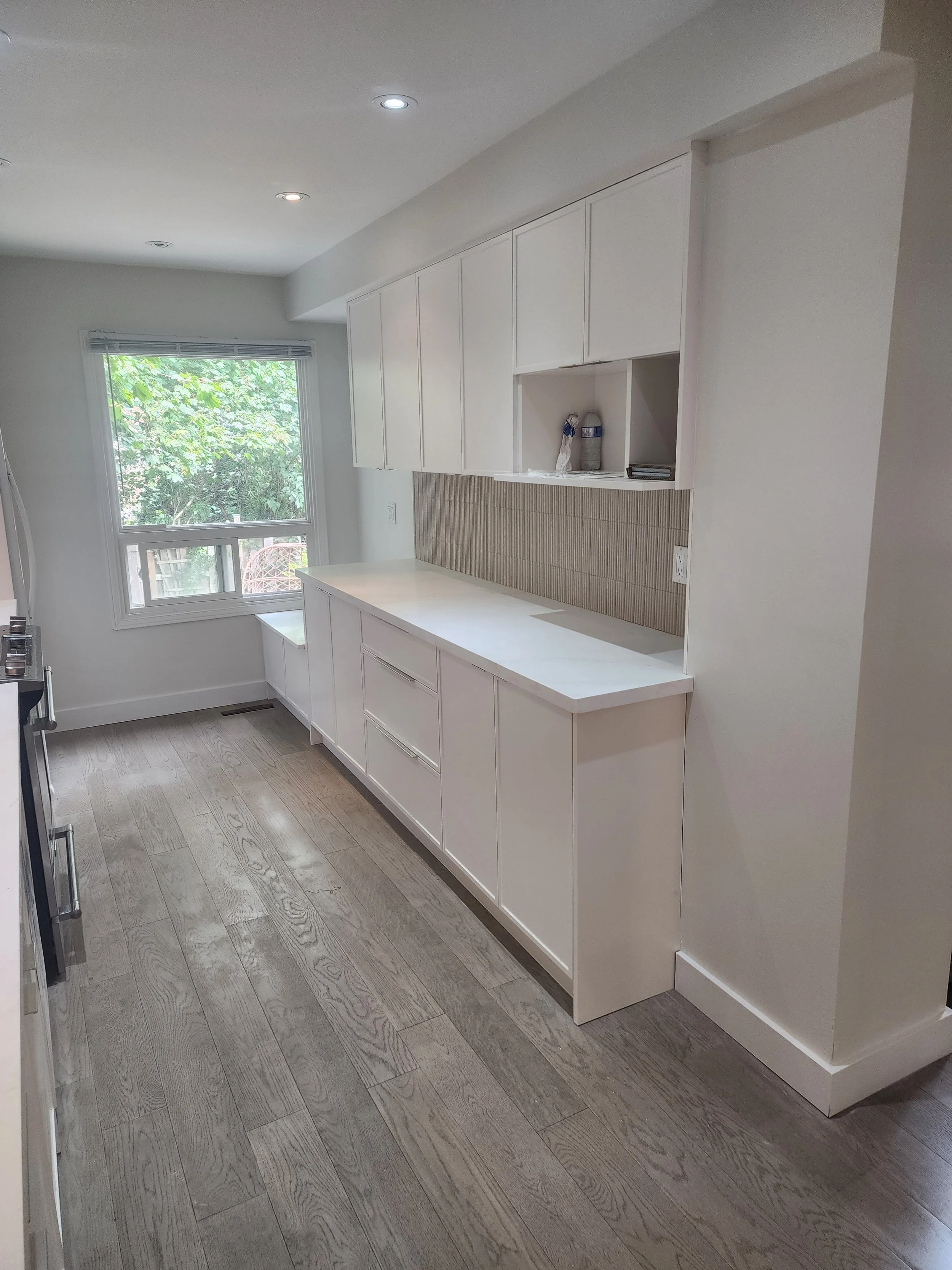 Clean kitchen with white cabinets, hardwood floor, window letting in natural light, and some items on open shelves.