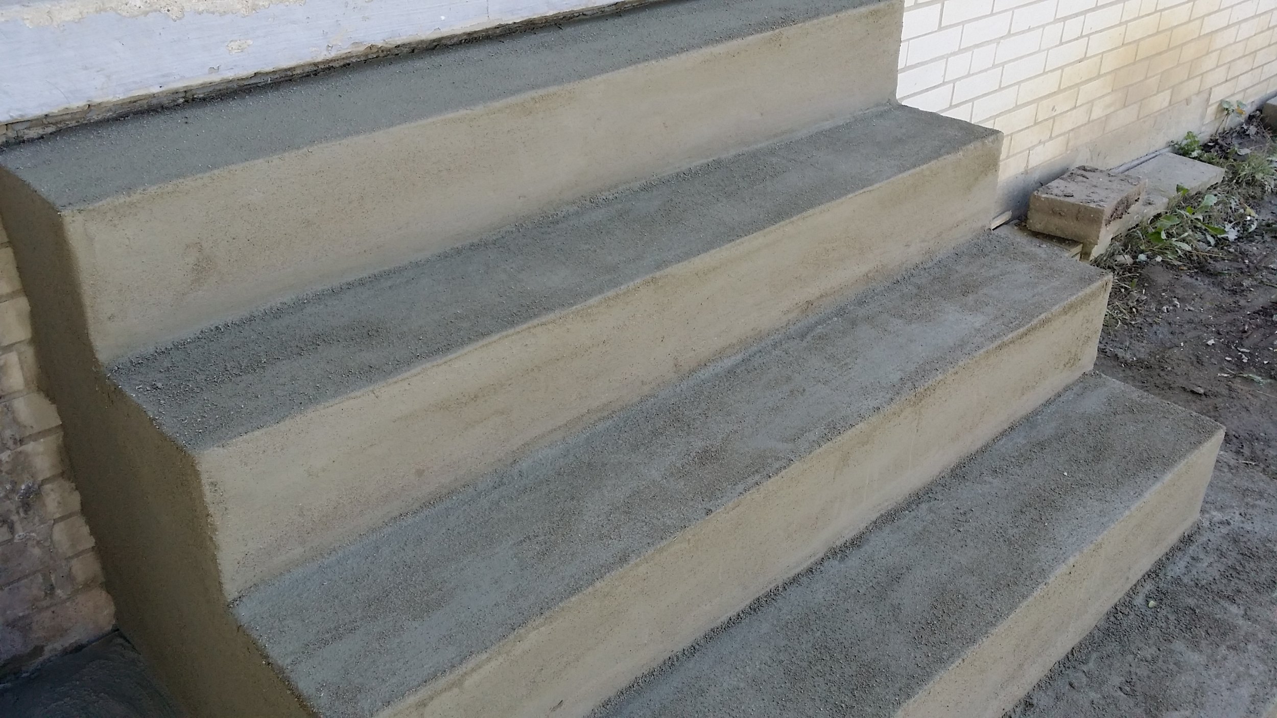 Concrete stairs under construction next to a brick wall and some dirt.