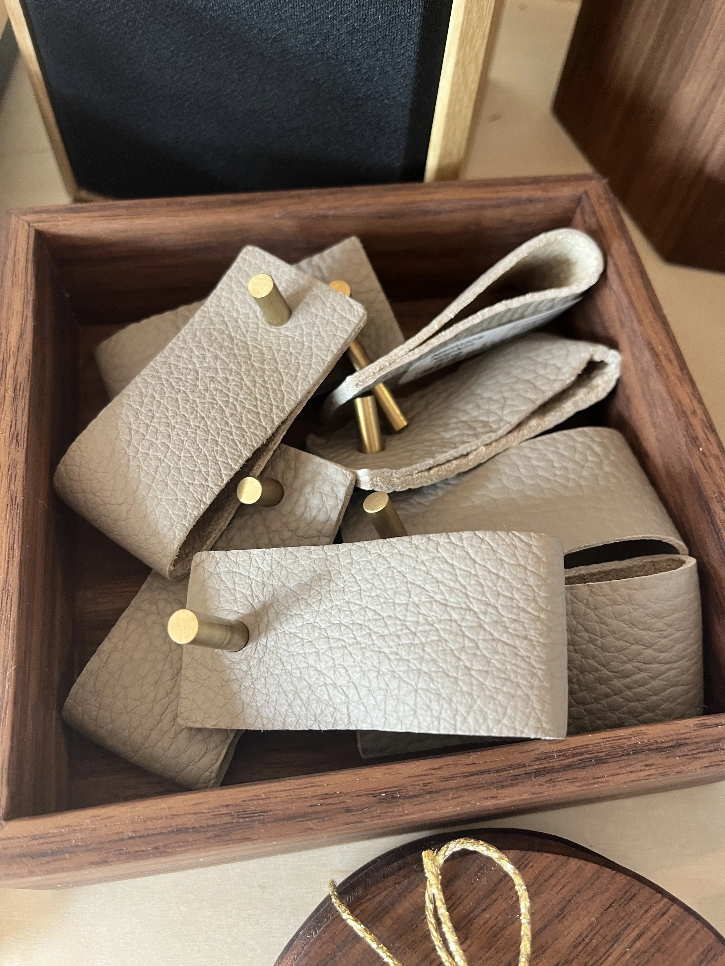 Multiple light grey leather napkin rings with brass displayed at Studio 304 in a wooden box