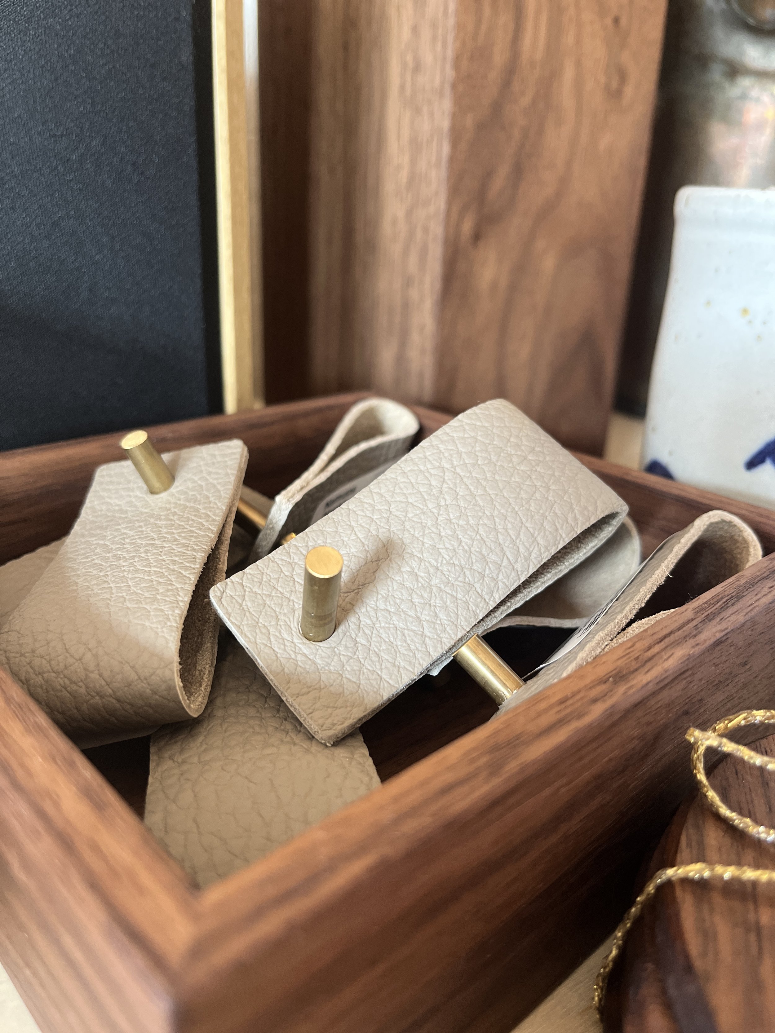Multiple light grey leather napkin rings with brass displayed at Studio 304 in a wooden box