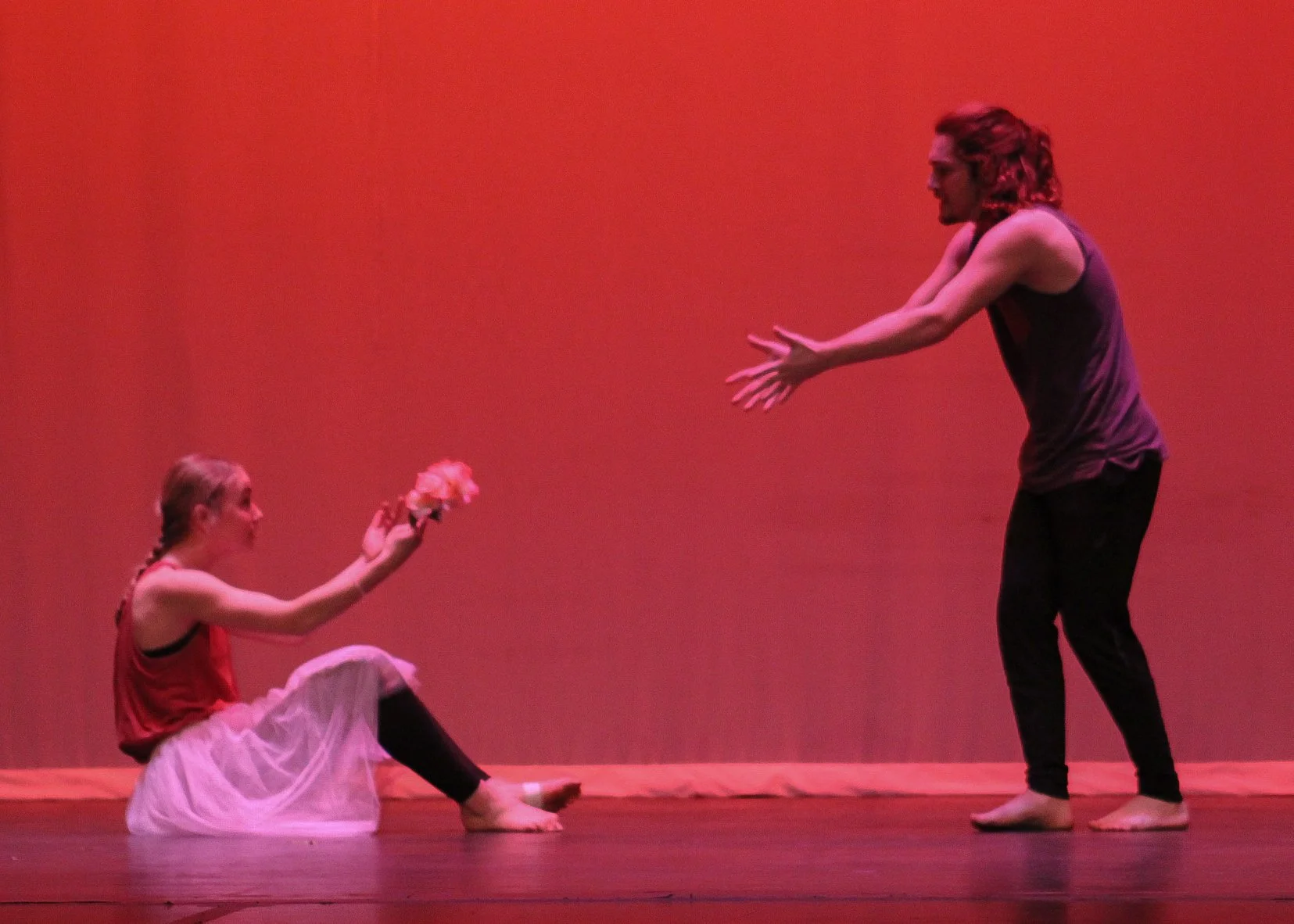A girl sitting on the floor handing a bouquet of flowers to a man standing on stage.