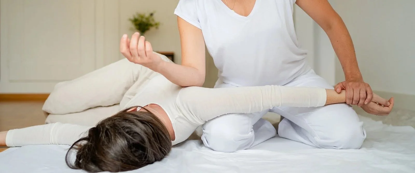 Junge Frau liegt auf Bauch, wird von einer Therapeutin im Yoga-Stil behandelt, im Schlafzimmer.