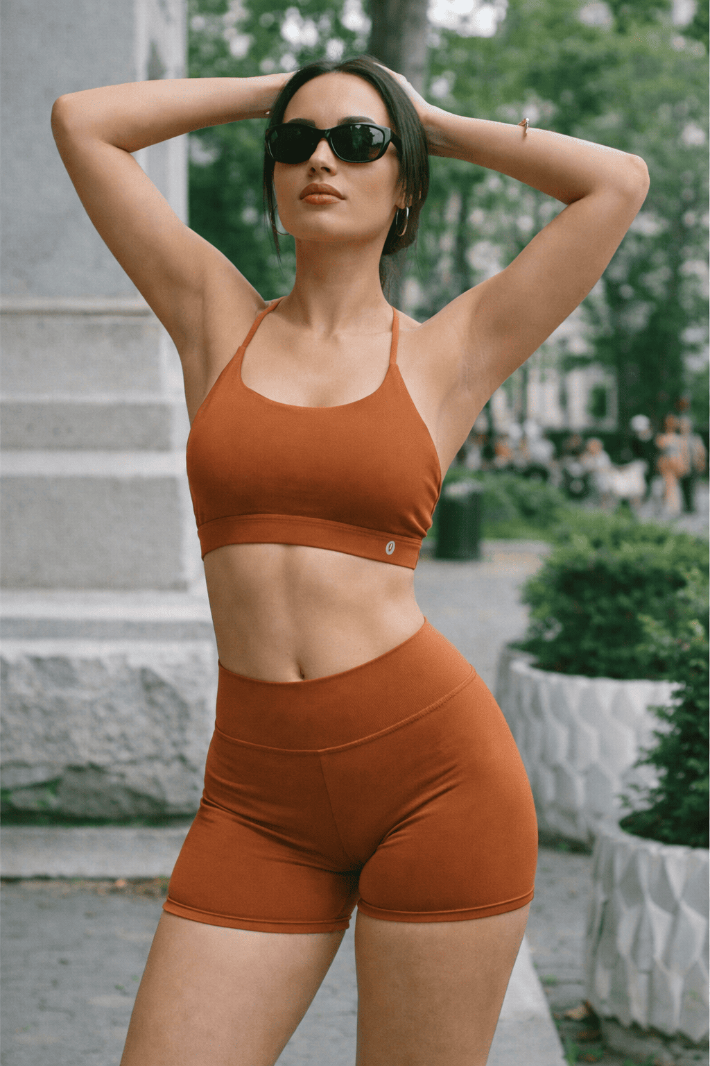 Mujer con gafas de sol, ropa deportiva naranja, posando al aire libre en la ciudad.