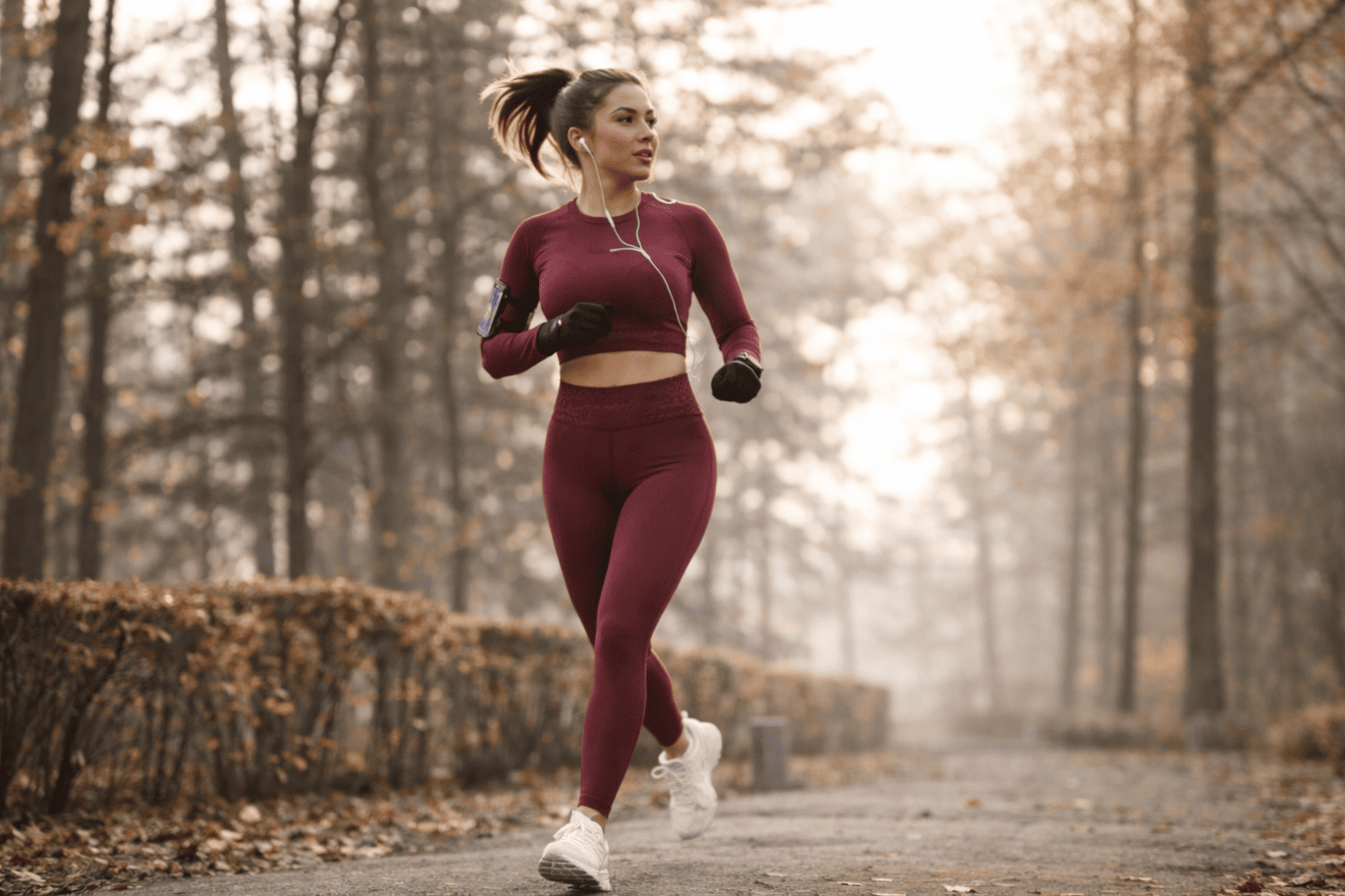 Mujer corriendo deportivamente en un sendero en un bosque con árboles con hojas otoñales, mientras viste un conjunto de ropa deportiva.