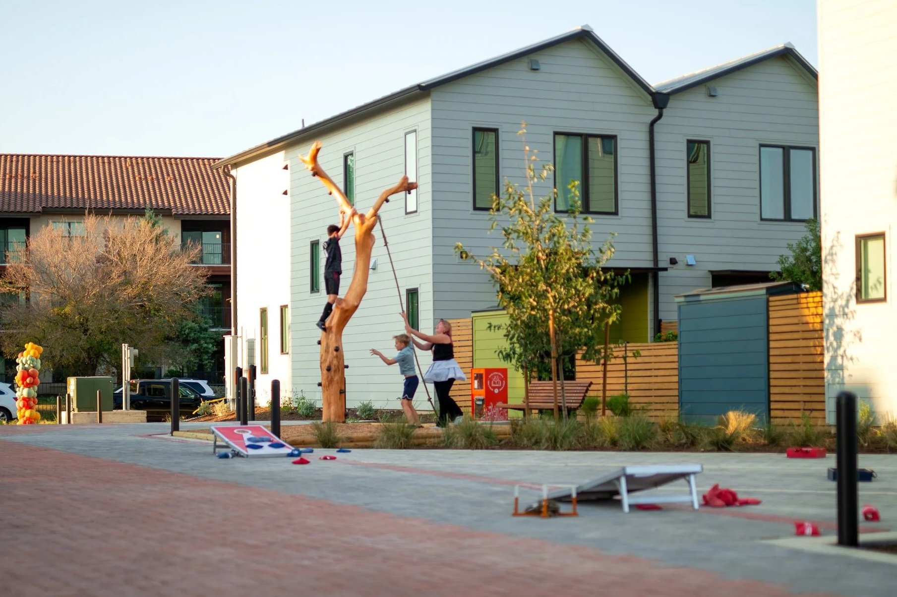 Children playing on a swing hanging from a tree in a modern residential area during late afternoon.