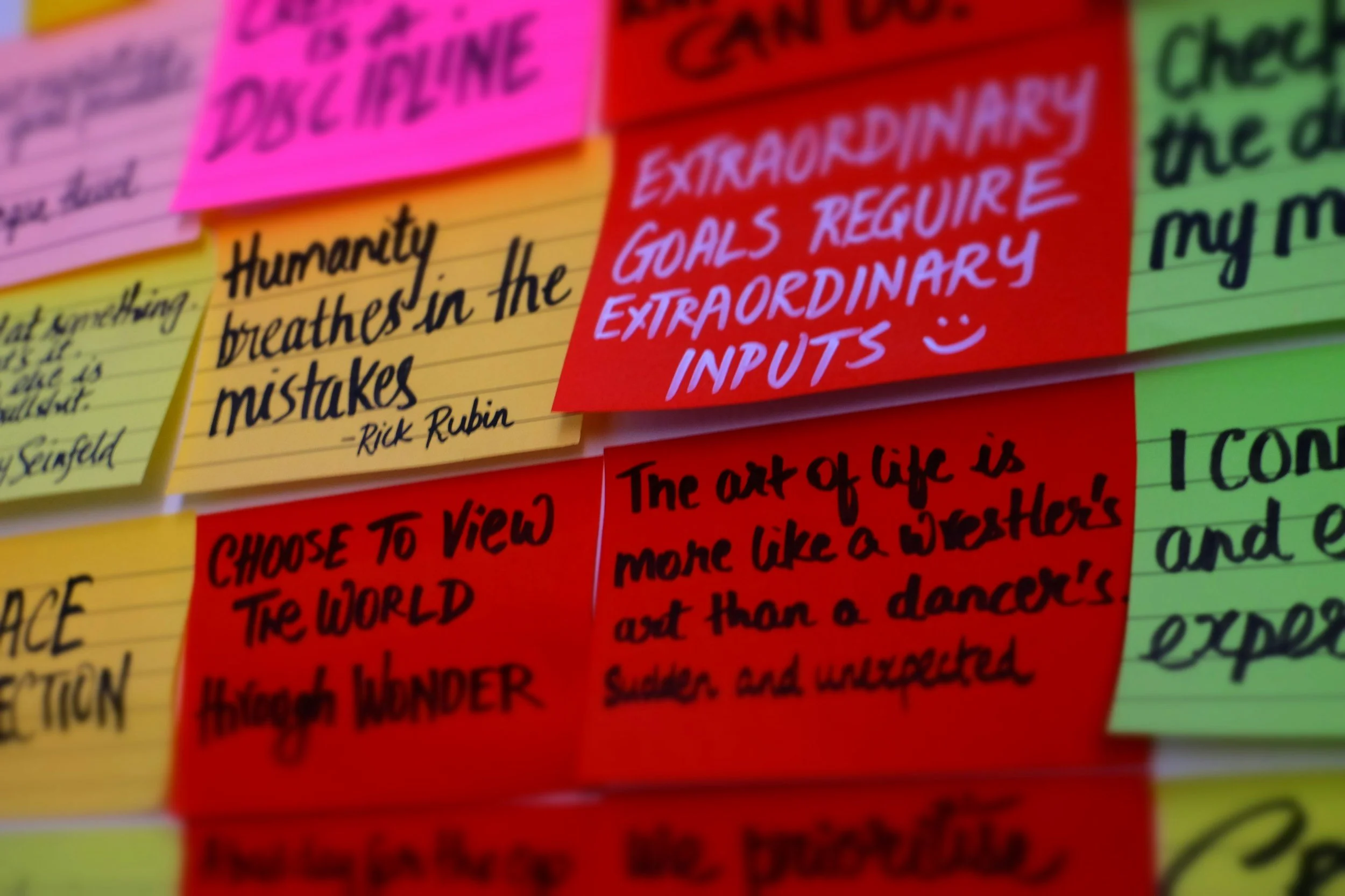 Colorful sticky notes on a wall with handwritten quotes and messages. The notes are in pink, red, yellow, and green, with quotes about life, goals, and philosophy.