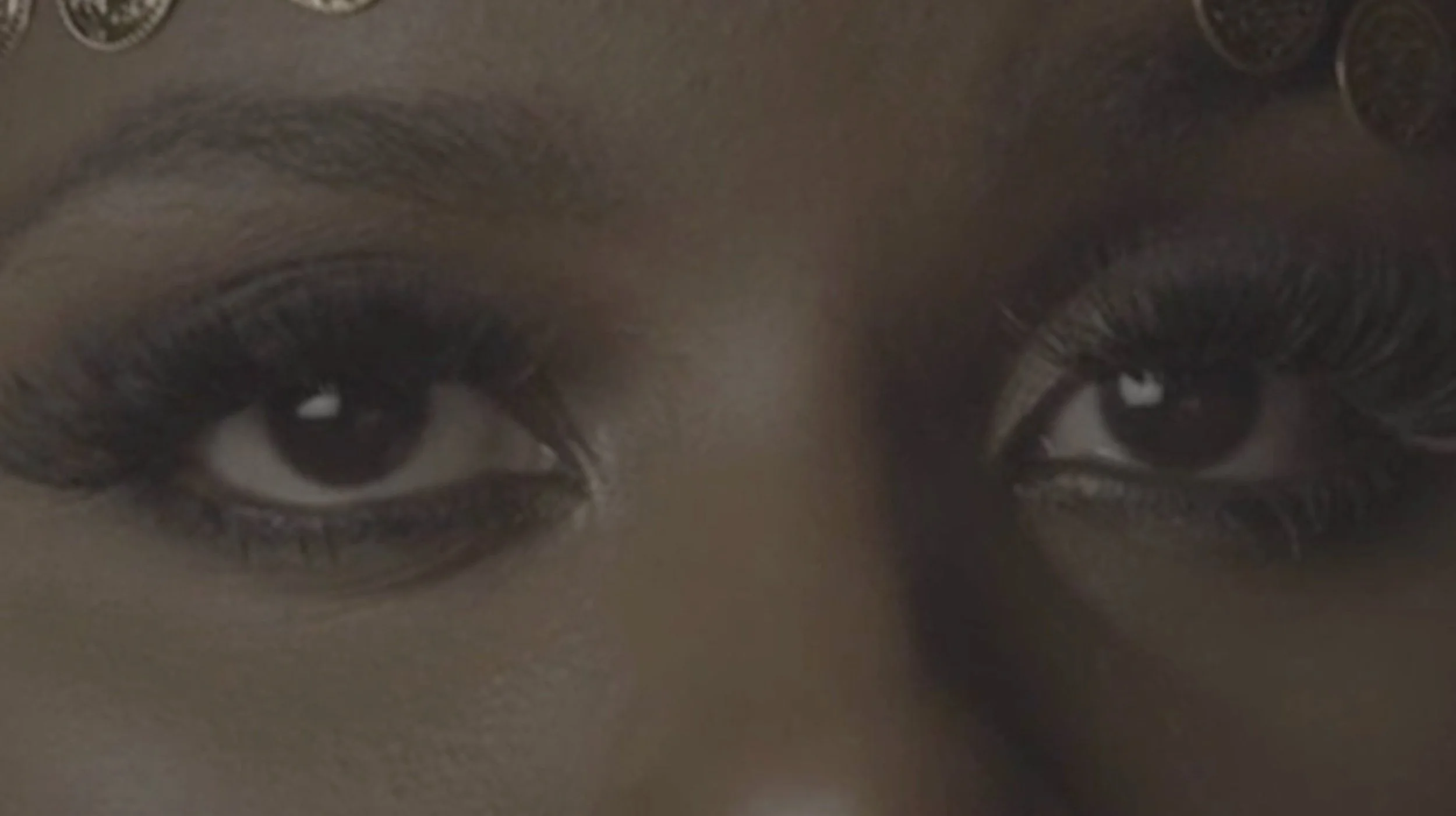 Close-up of a person's eyes with dark makeup and decorative elements on the forehead.