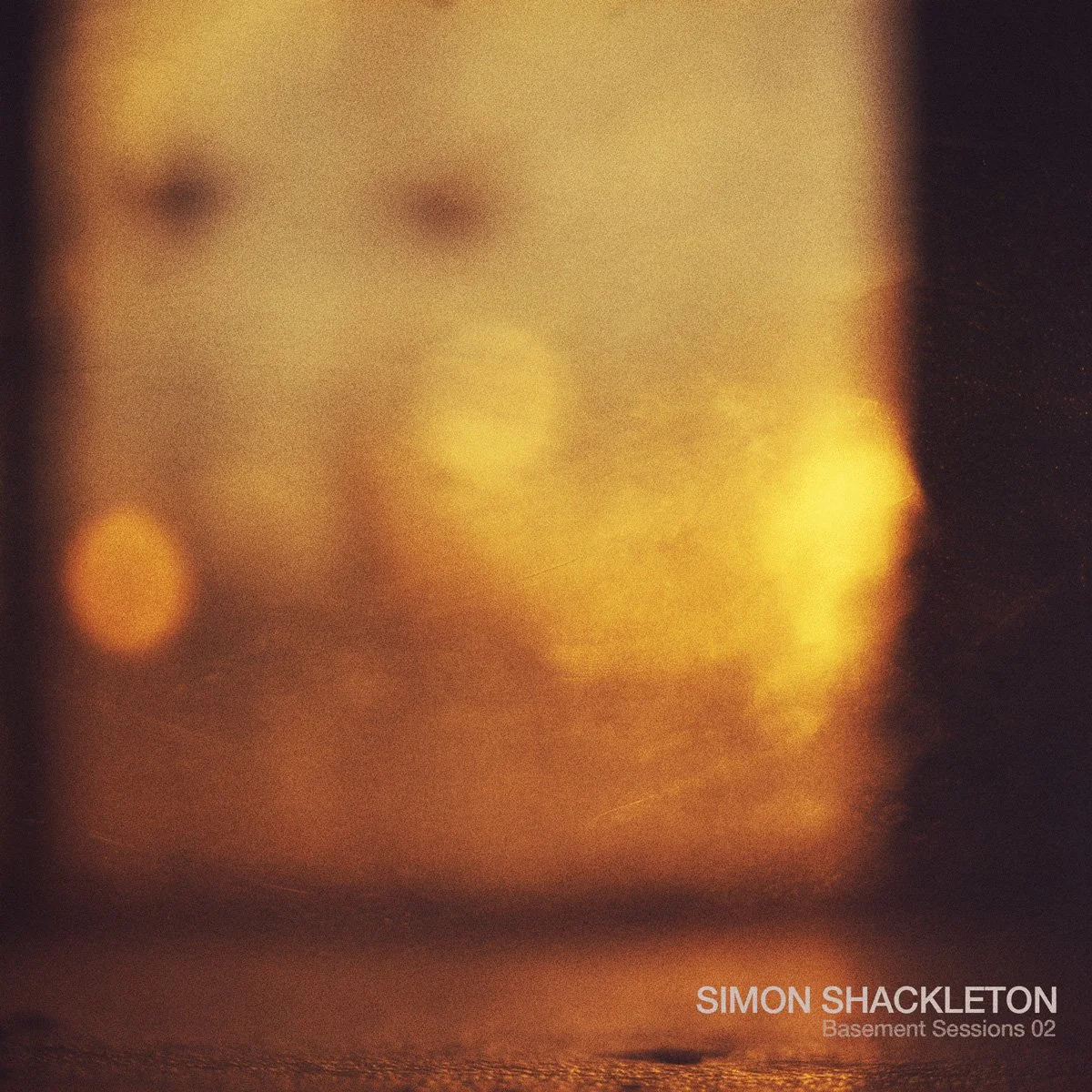 Simon Shackleton Basement Sessions 02 artwork featuring warm amber tones, blurred lights, and grainy atmospheric texture evoking a late-night underground mood