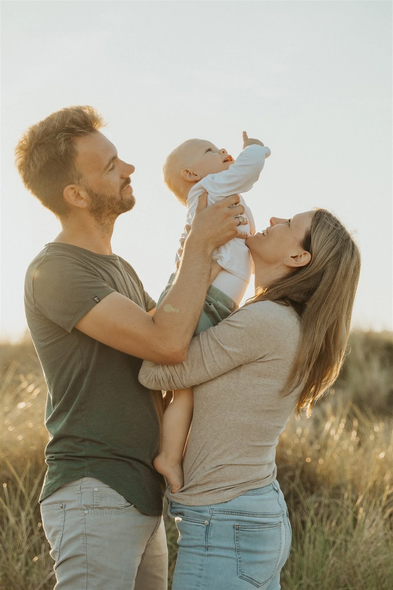 Ein Paar hält ein lachendes Baby in den Armen, während sie im Freien bei Sonnenuntergang stehen.