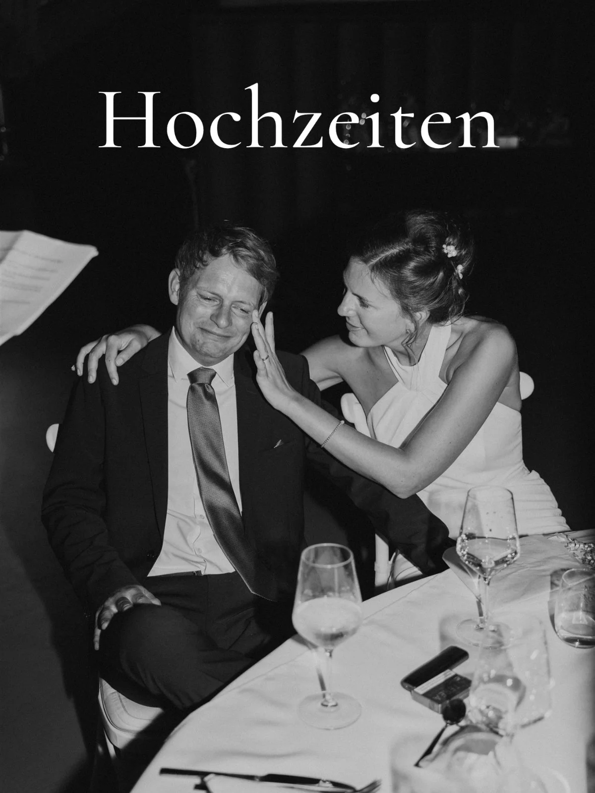 Zwei Menschen bei einer Hochzeit, der Mann sitzt mit geschlossenen Augen, die Frau streichelt sein Gesicht, beide lachen.