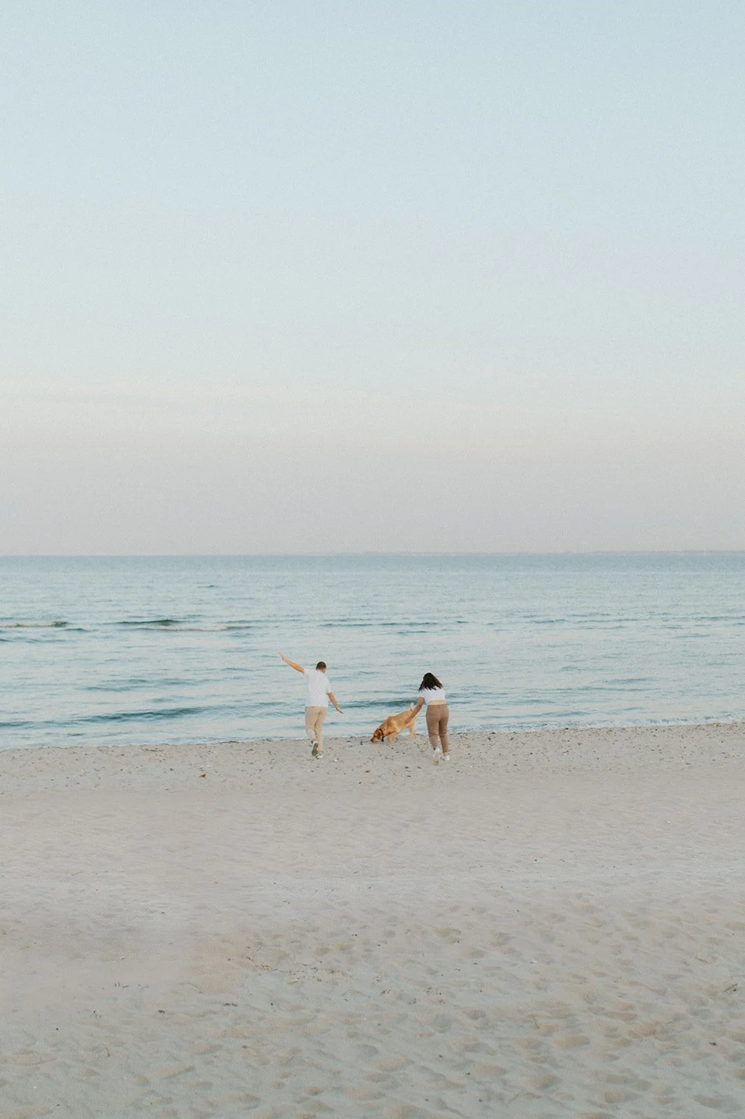 Zwei Personen und ein Hund am Strand, Blick auf das Meer bei Sonnenuntergang.