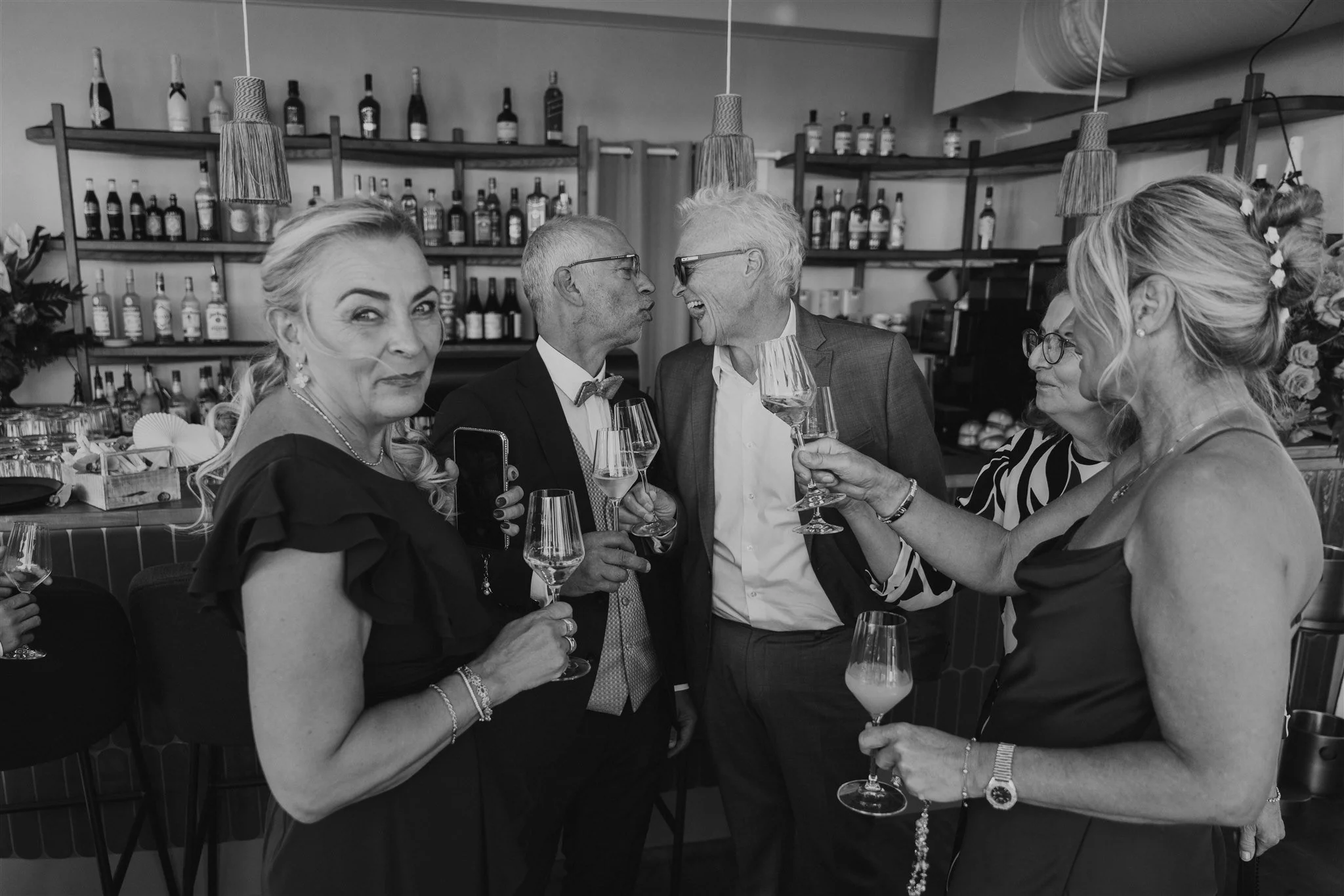 Eine Gruppe älterer Menschen bei einer Hochzeit im Soul Grömitz, die sich unterhalten, Spaß haben und Wein trinken, mit Flaschen im Hintergrund.