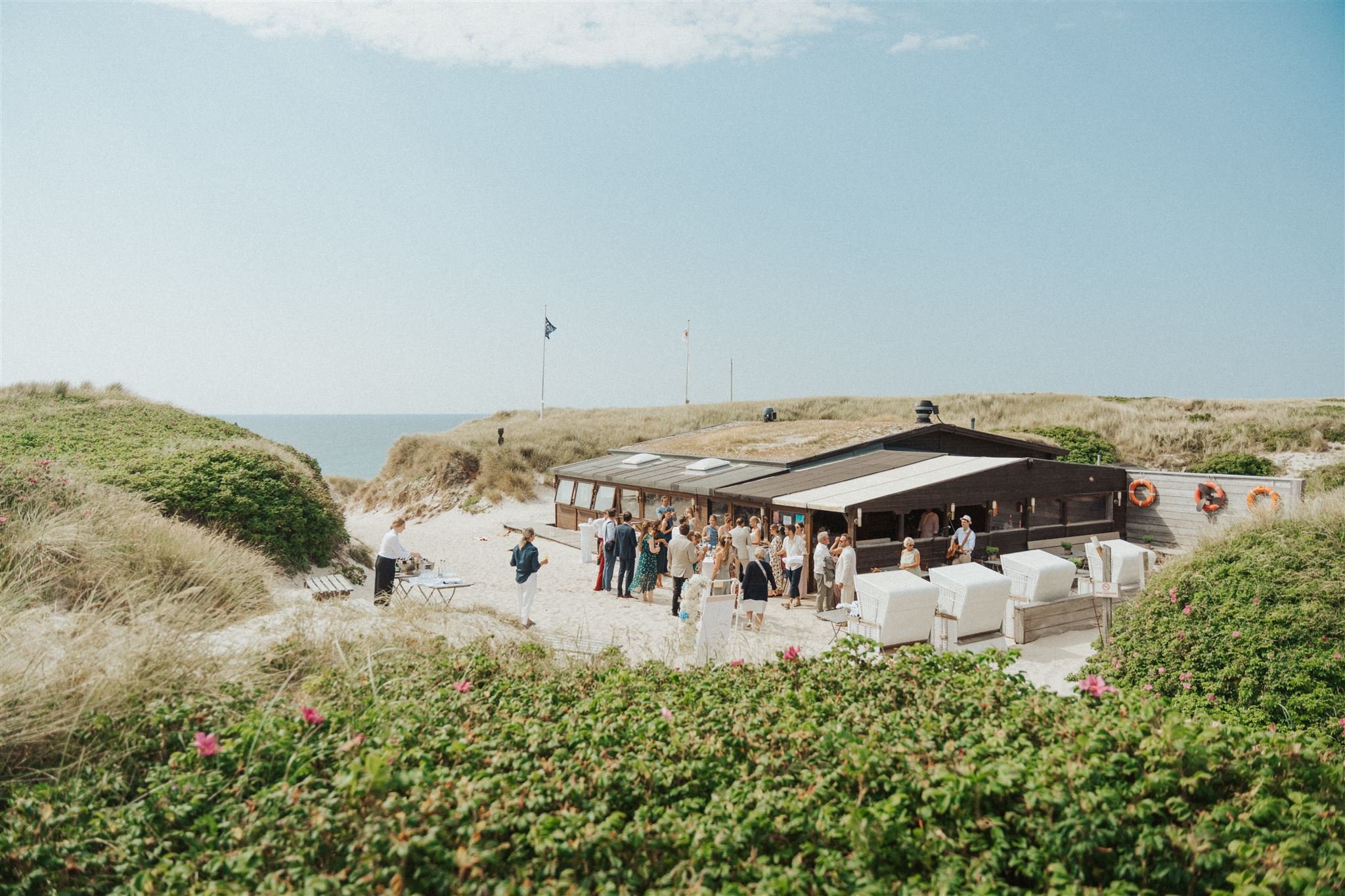 Sommerhochzeit auf Sylt im Restaurant Kap-Horn, direkt am Strand, umgeben von Dünen versammelt sich die Hochzeitsgesellschaft bei sonnigem Wetter draußen.