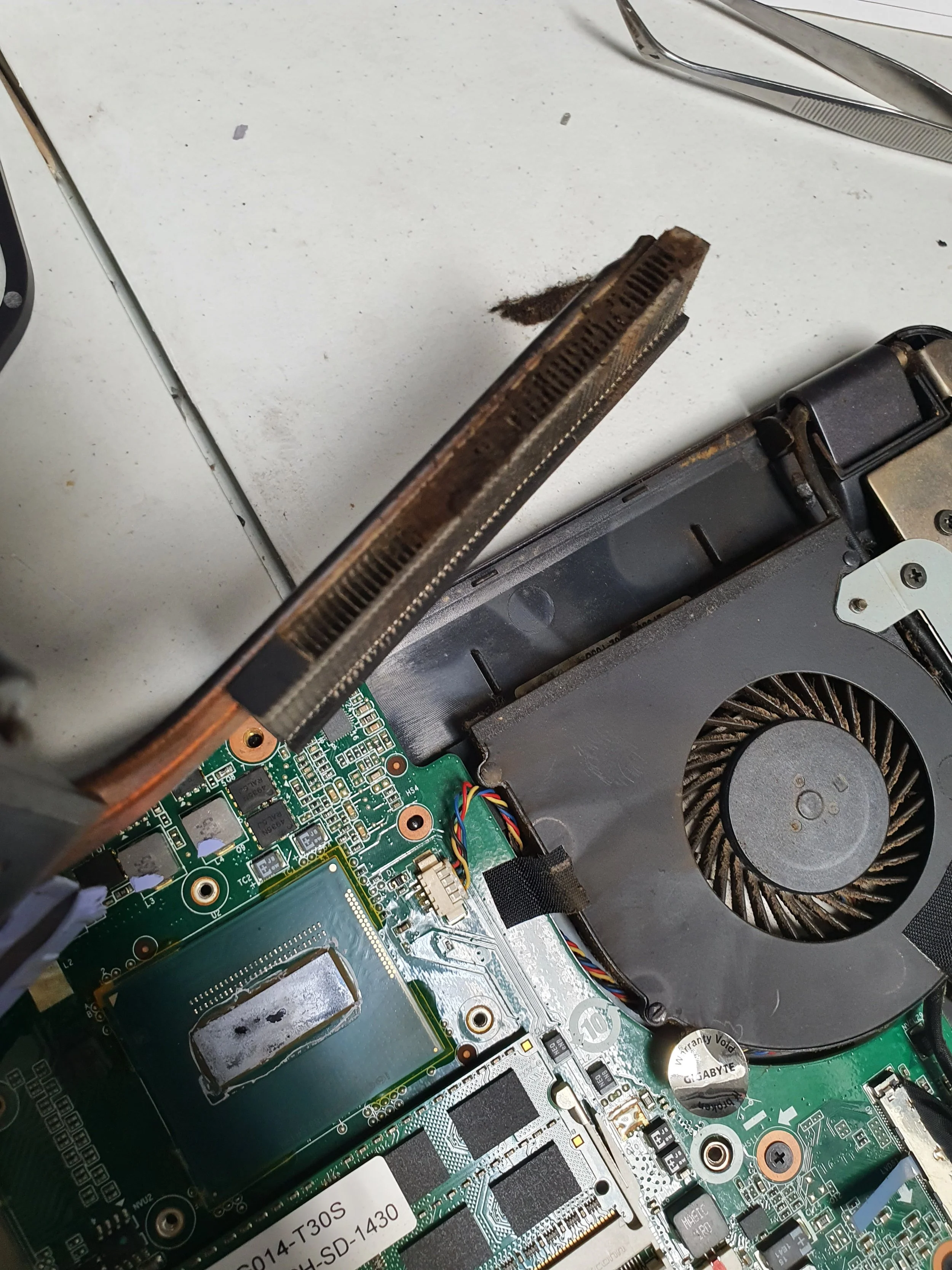 Inside an open laptop, showing the cooling fan, motherboard with various chips, and heat sink with dust.