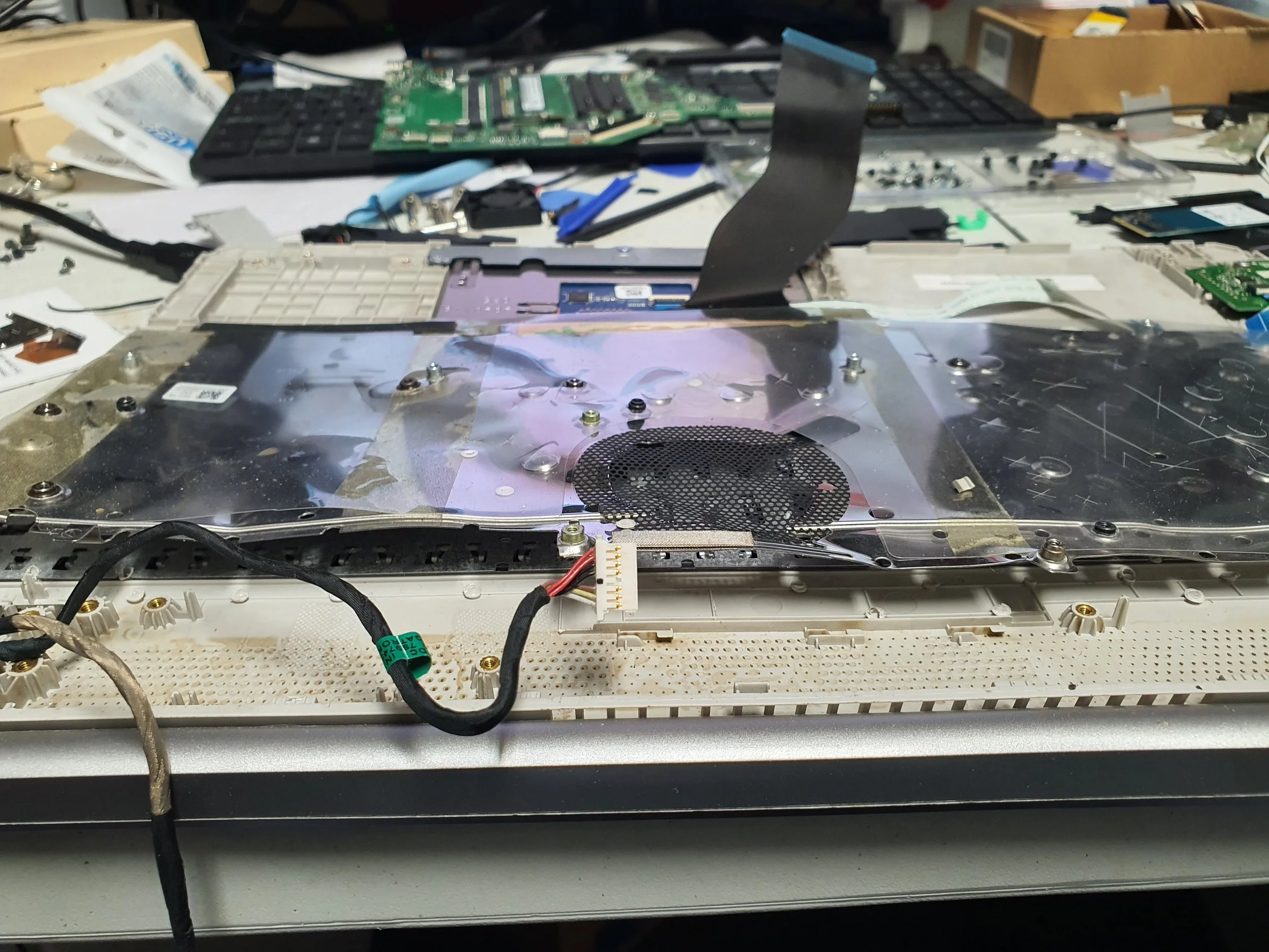 Disassembled laptop with internal components exposed on a cluttered worktable.