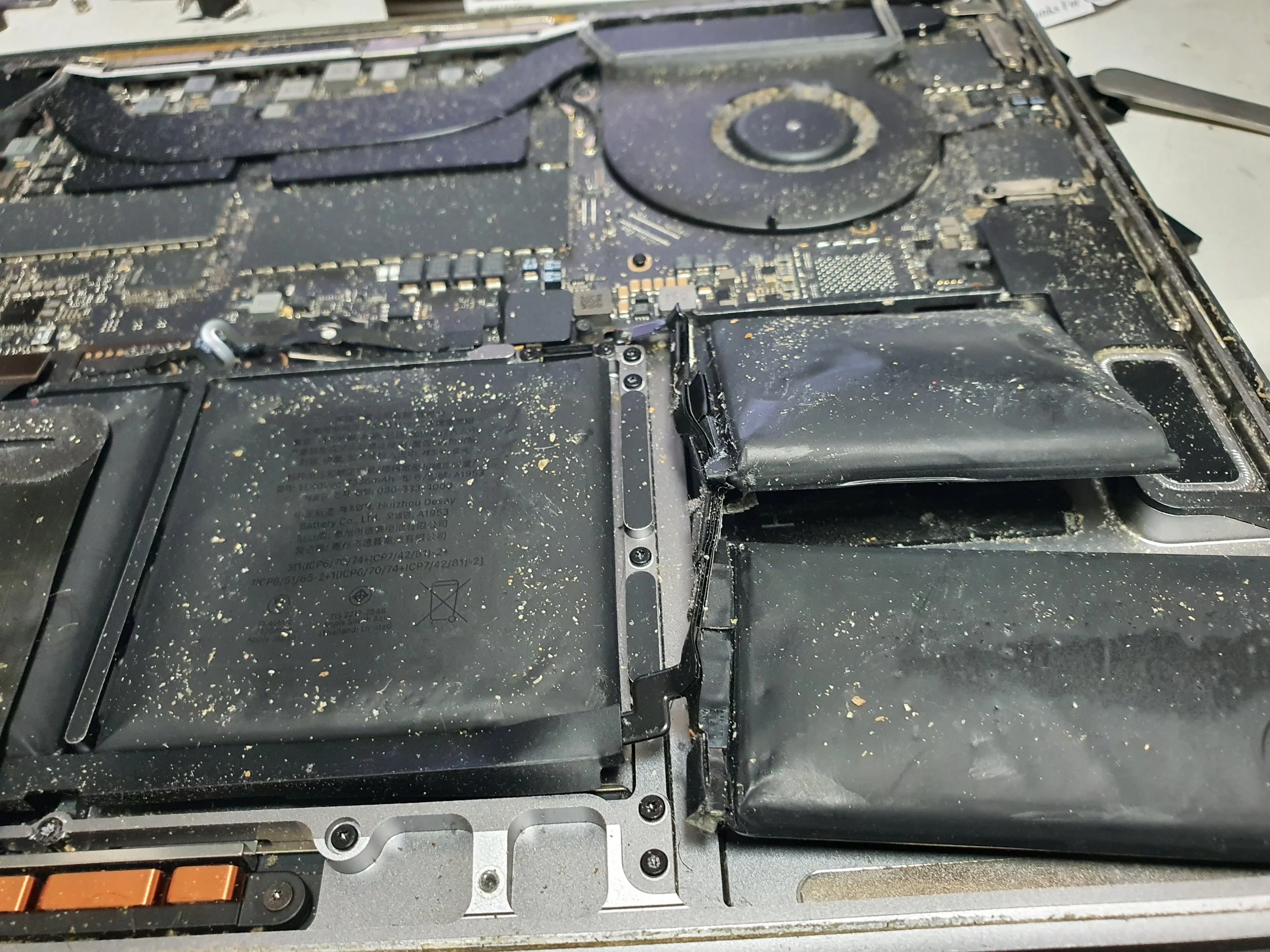 Open laptop with the back cover removed, showing internal components like the battery and circuit board, covered in dust and debris.