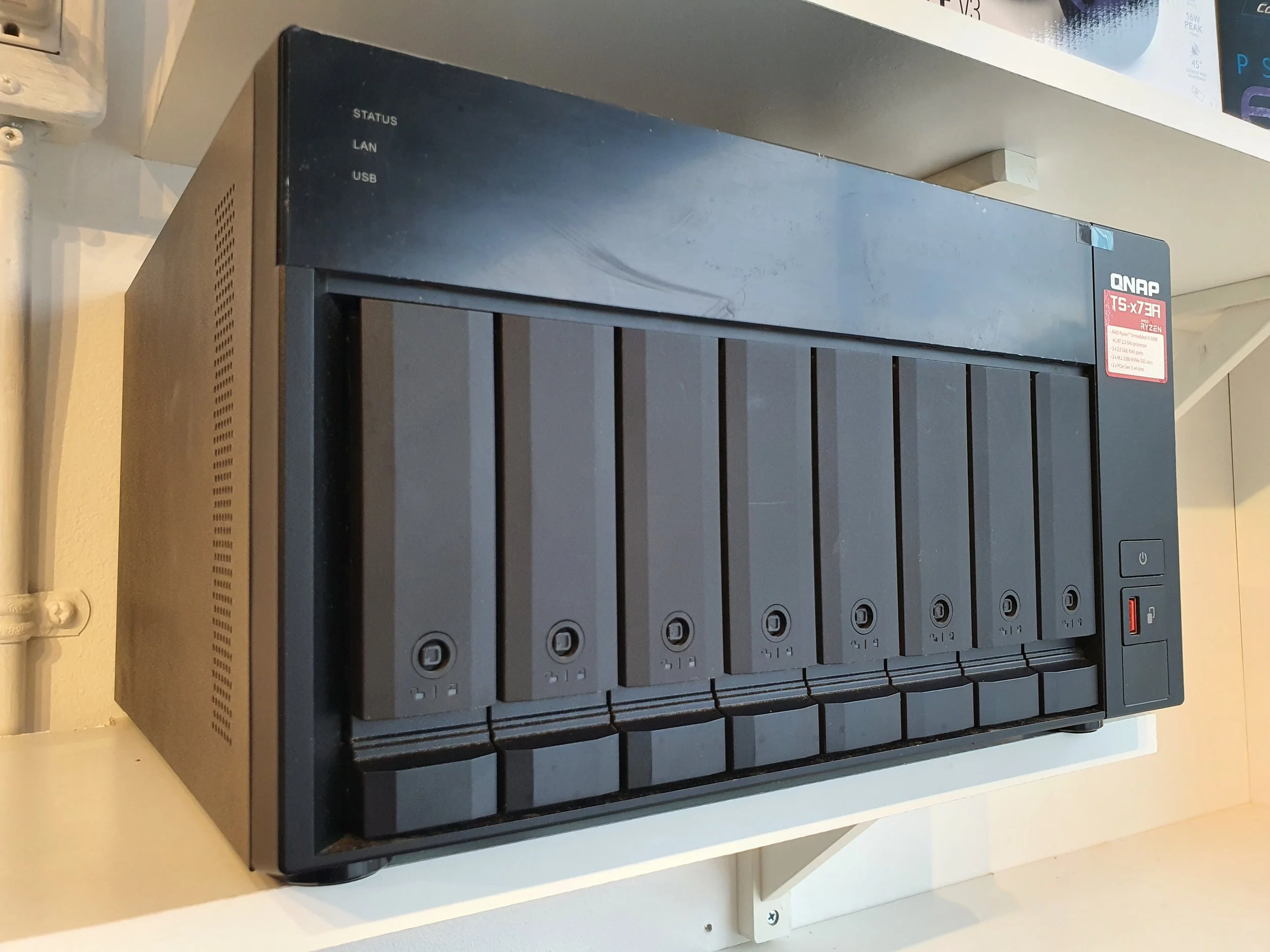 QNAP Network Attached Storage (NAS) device with multiple drive bays, located on a white shelf.