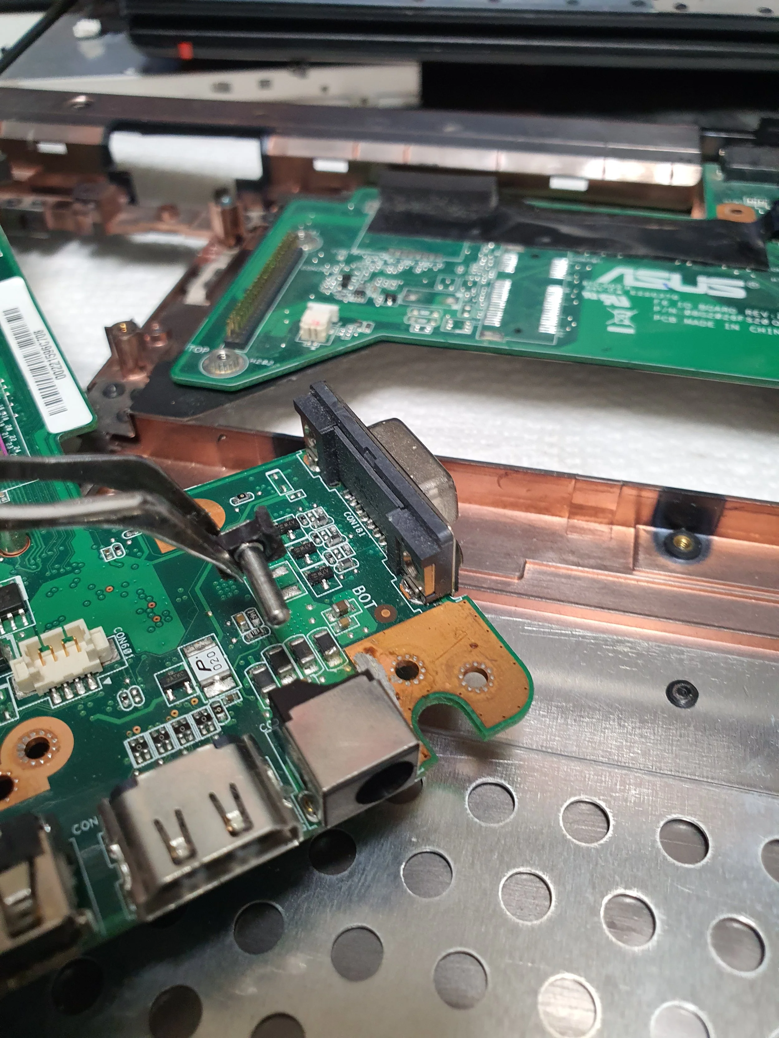 Close-up of disassembled circuit boards inside a laptop, with visible ports, connectors, and electronic components, on a perforated metallic surface.