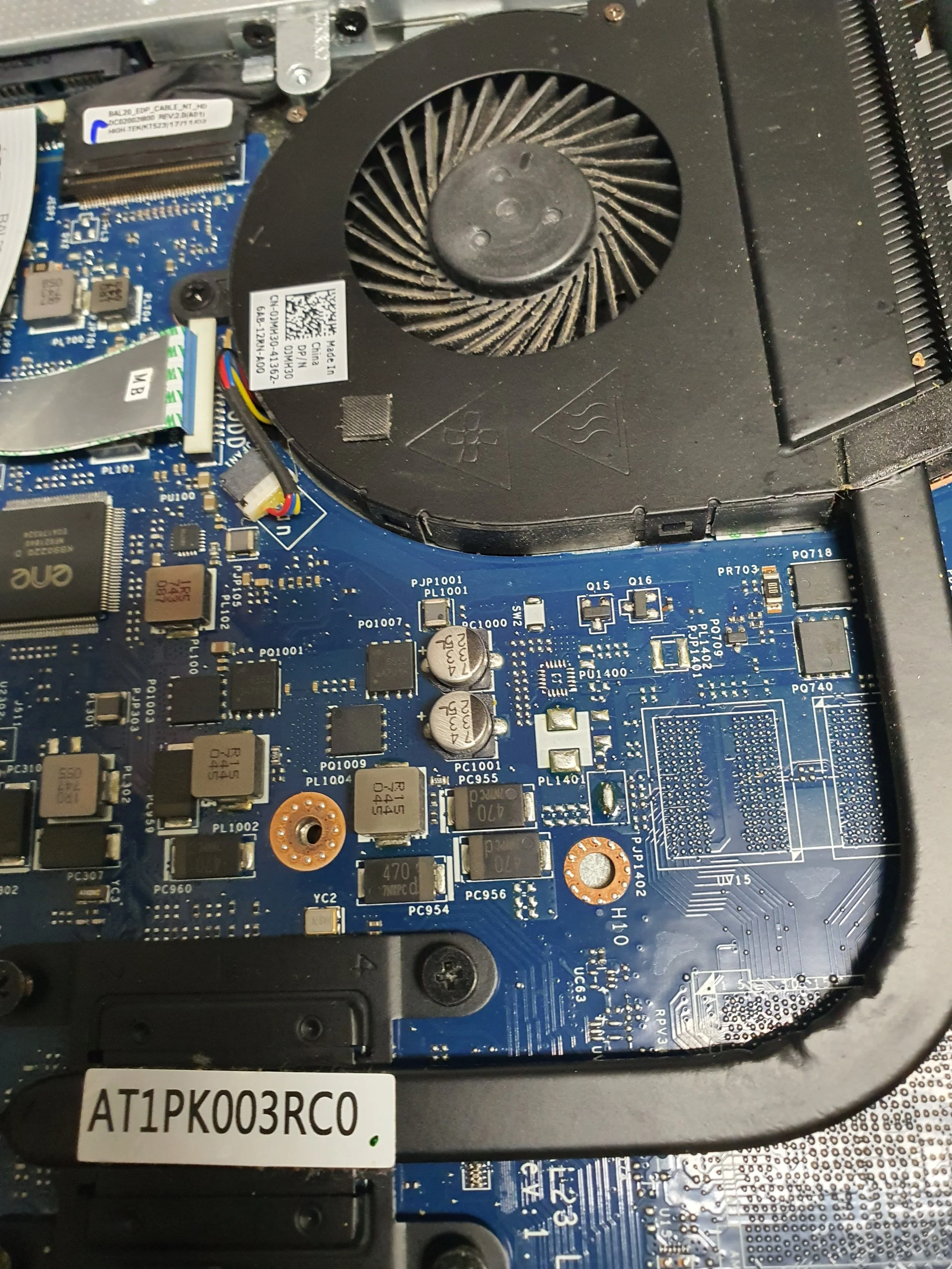 Close-up of a laptop's internal blue circuit board with various chips, capacitors, and connectors, featuring a cooling fan at the top.