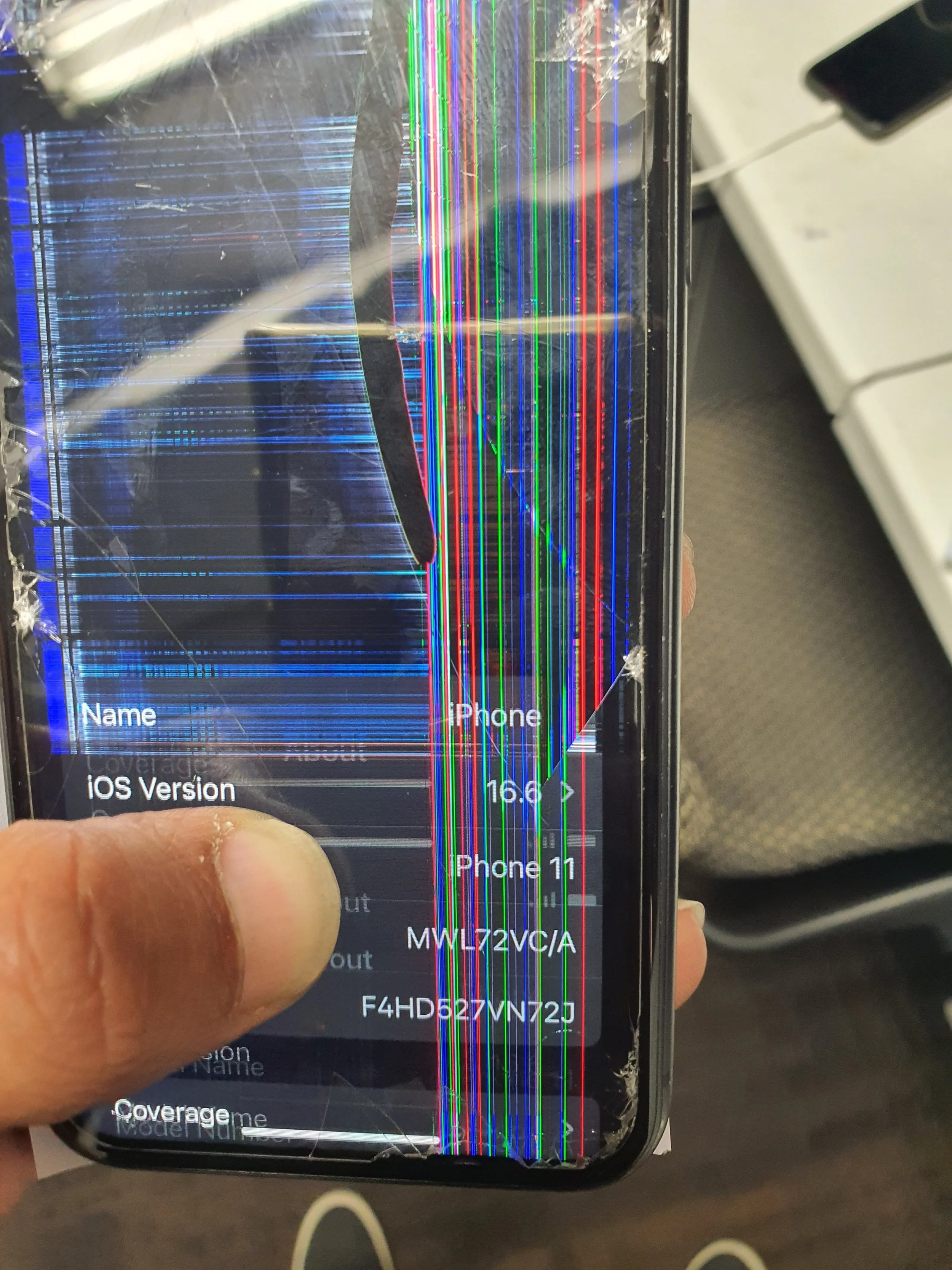 A broken smartphone with a screen that has extensive vertical and horizontal colorful lines and cracks.