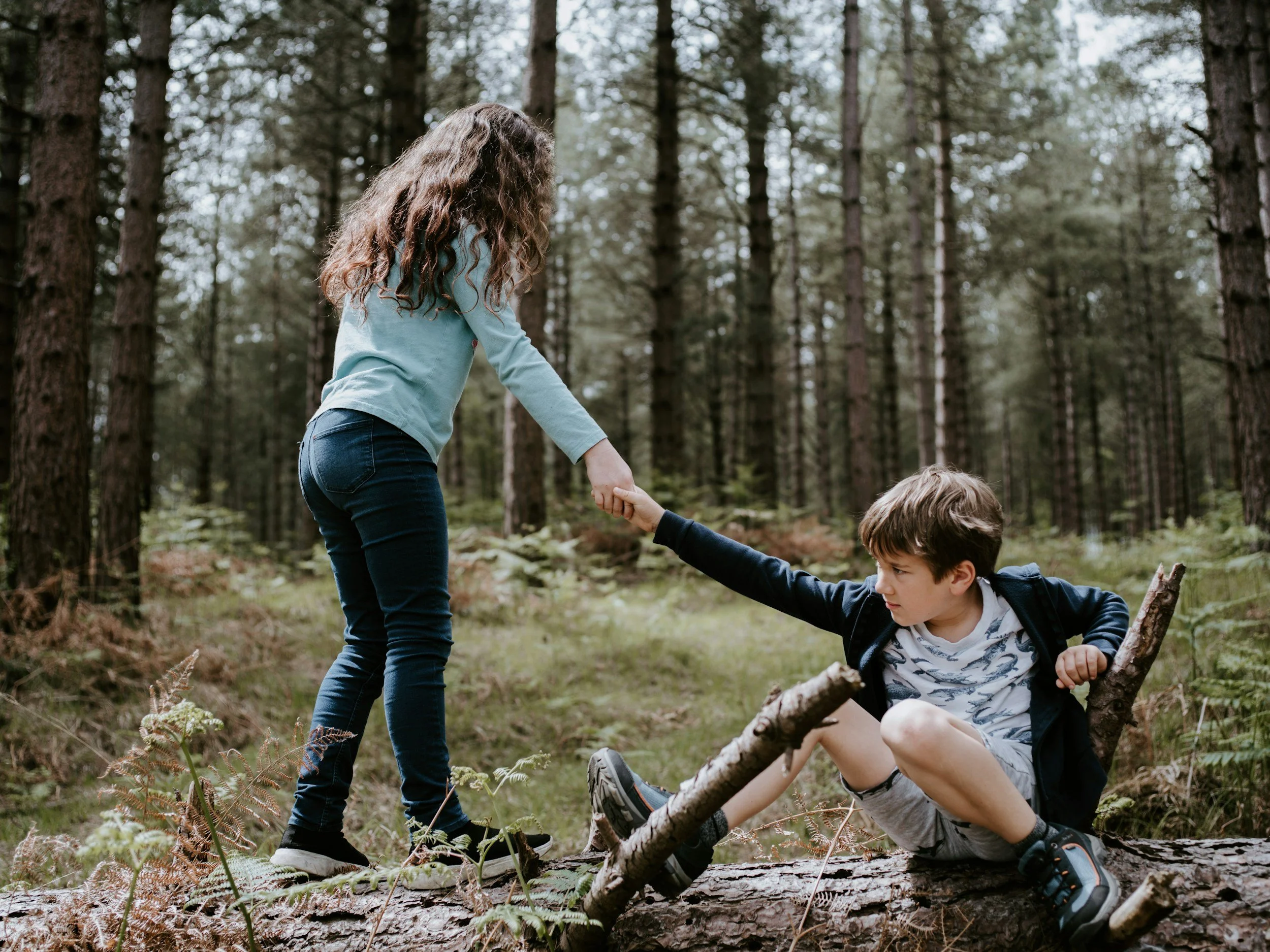 Model girl helping model boy up on a log, envisioned to be playing in the wilderness of Wyoming.