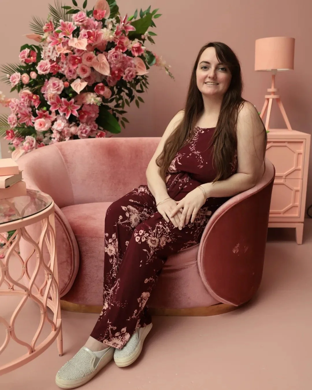 Cozykins Plushies' Founder, Alexis Berardi-Hawley, at the 2024 Entreprenista Convention at The Ritz in Florida. Alex's long auburn hair is down, they are sat on a pink set with pink florals in the background. Alex is in a red/pink floral jumpsuit.