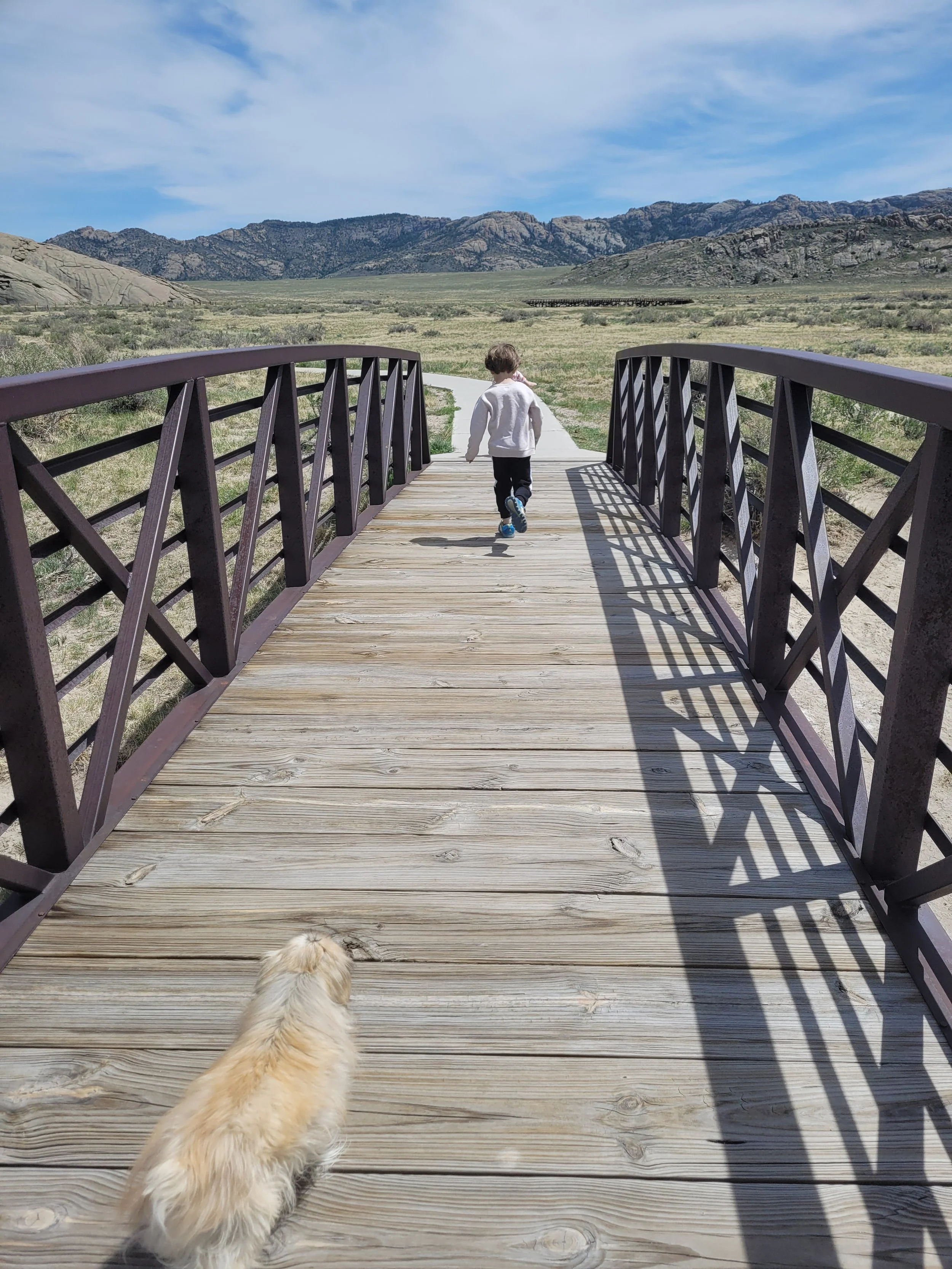 A boy running across a bridge, followed by the family pekingese Paris, in Natrona County, Wyoming.