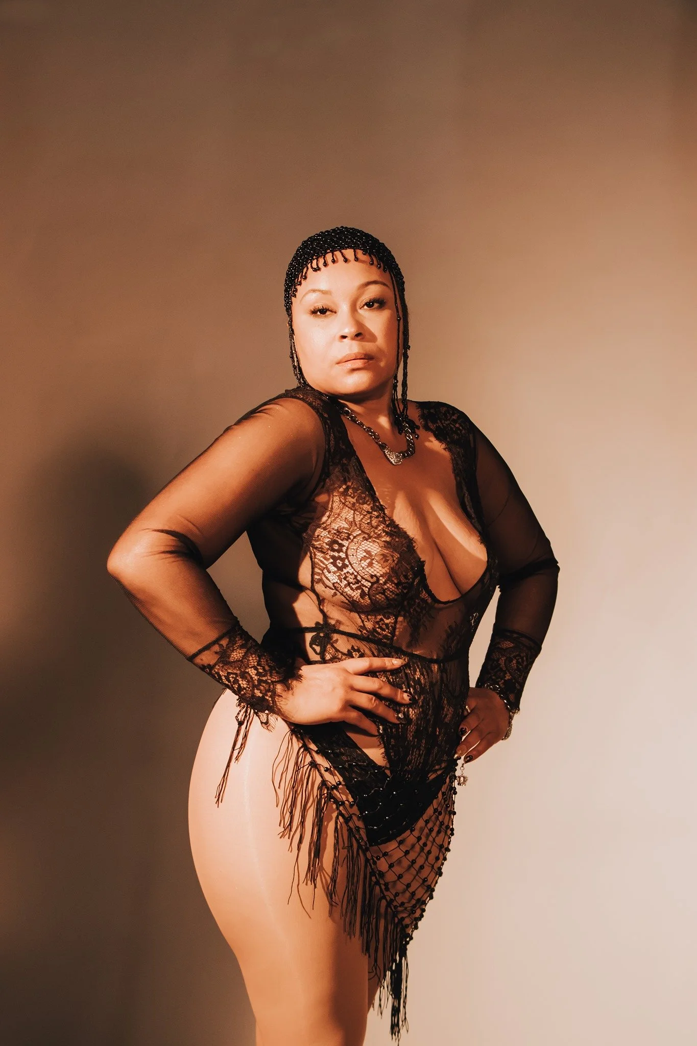 SHEMA of Austin, TX hip hop/RnB artist. A Black woman adorned in black lace, beads, and tassels gazes into the camera, the whole image of sepia tones.