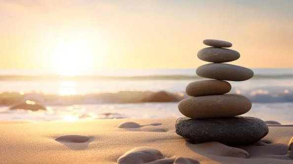 Stack of balanced stones on a peaceful beach at sunrise, representing Zen meditation, mindfulness, inner balance, and relaxation.