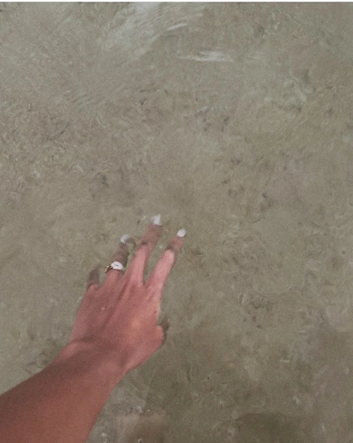 A person's hand with a ring on the ring finger touching a beige marble floor.