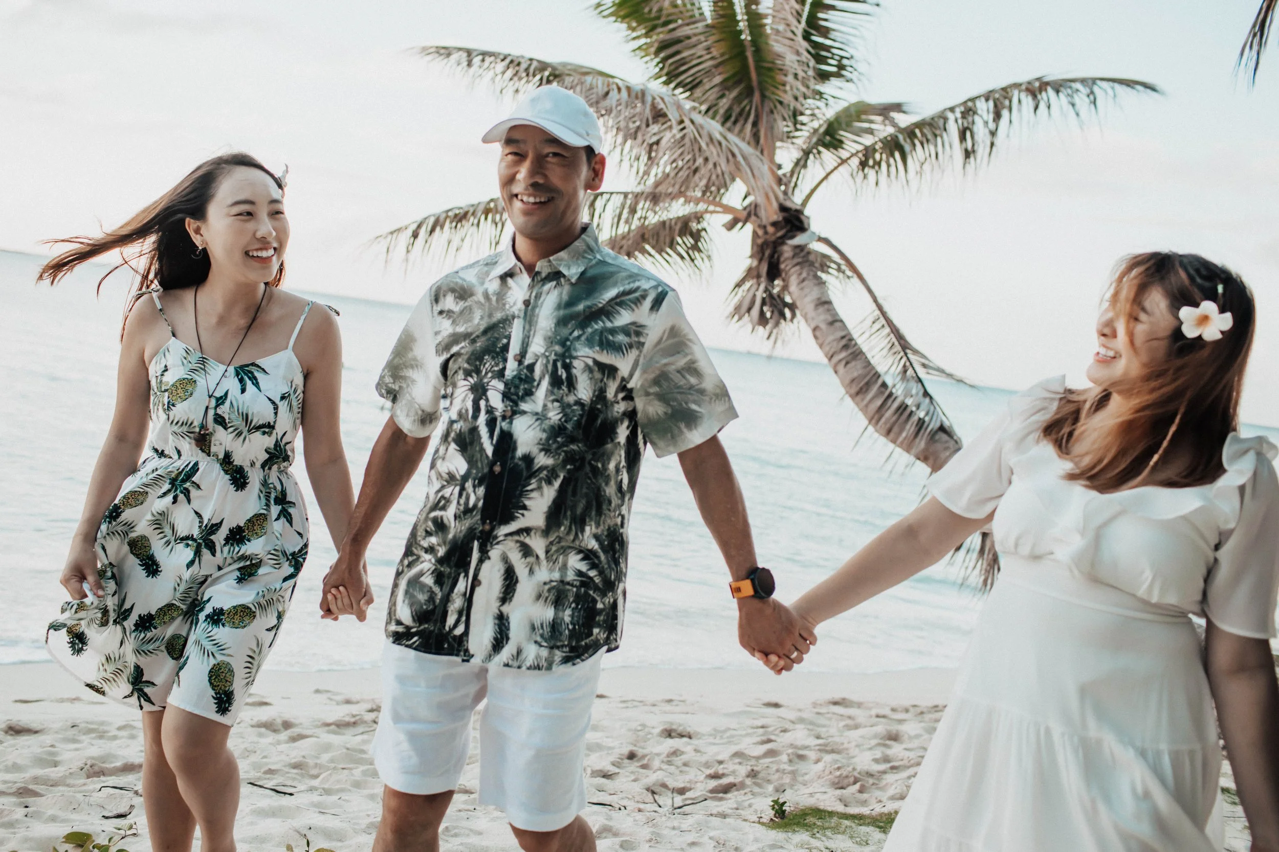 Three people holding hands and smiling on a beach with palm trees in the background