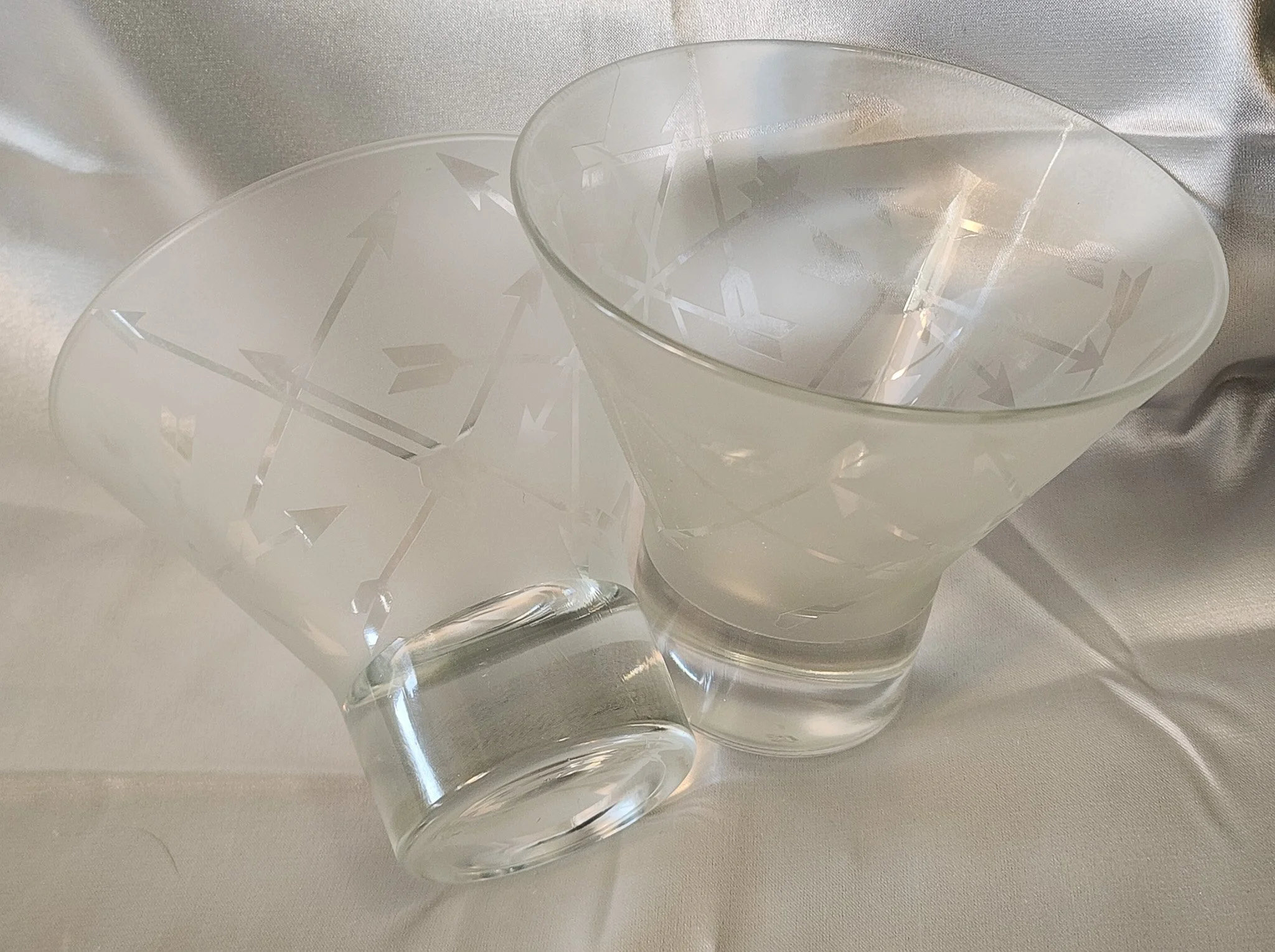 Broken frosted glass vase with arrow design, showing a large piece and a main body, placed on a textured orange and brown surface.
