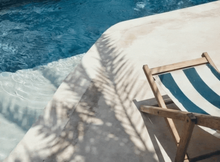 A poolside scene with a lounge chair featuring blue and white stripes, casting a shadow on the surrounding area.