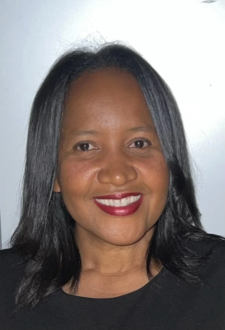 Close-up photo of a woman with black hair, smiling, wearing red lipstick, black top, against a plain light background.