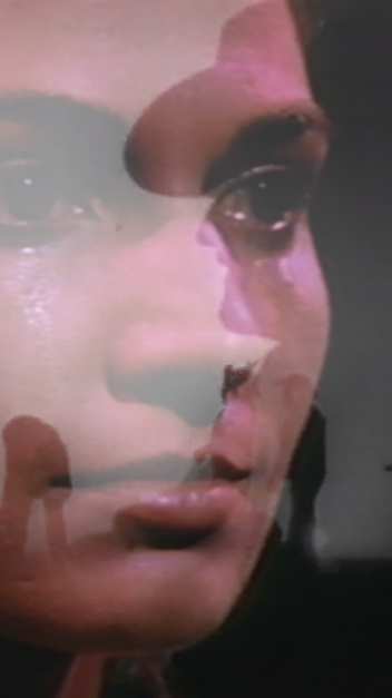A still image from one of the videos in Amanda Rose's Oracular series. An image of a feminine person's teary, unblinking eyes overlayed with the outline of a  masculine person smoking a cigarette and wearing a large cowboy hat