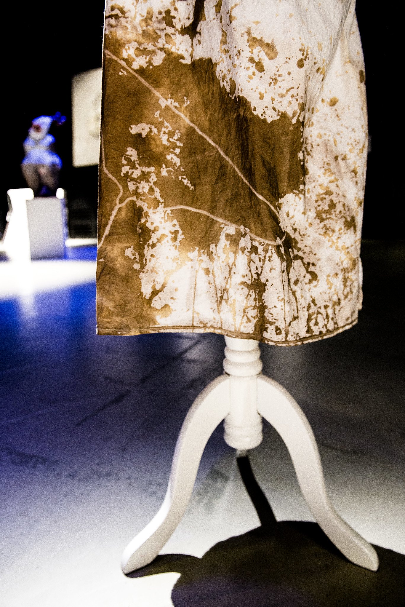 The lower half of a brown-stained hospital gown, the outline of a hanger is visible in the stain