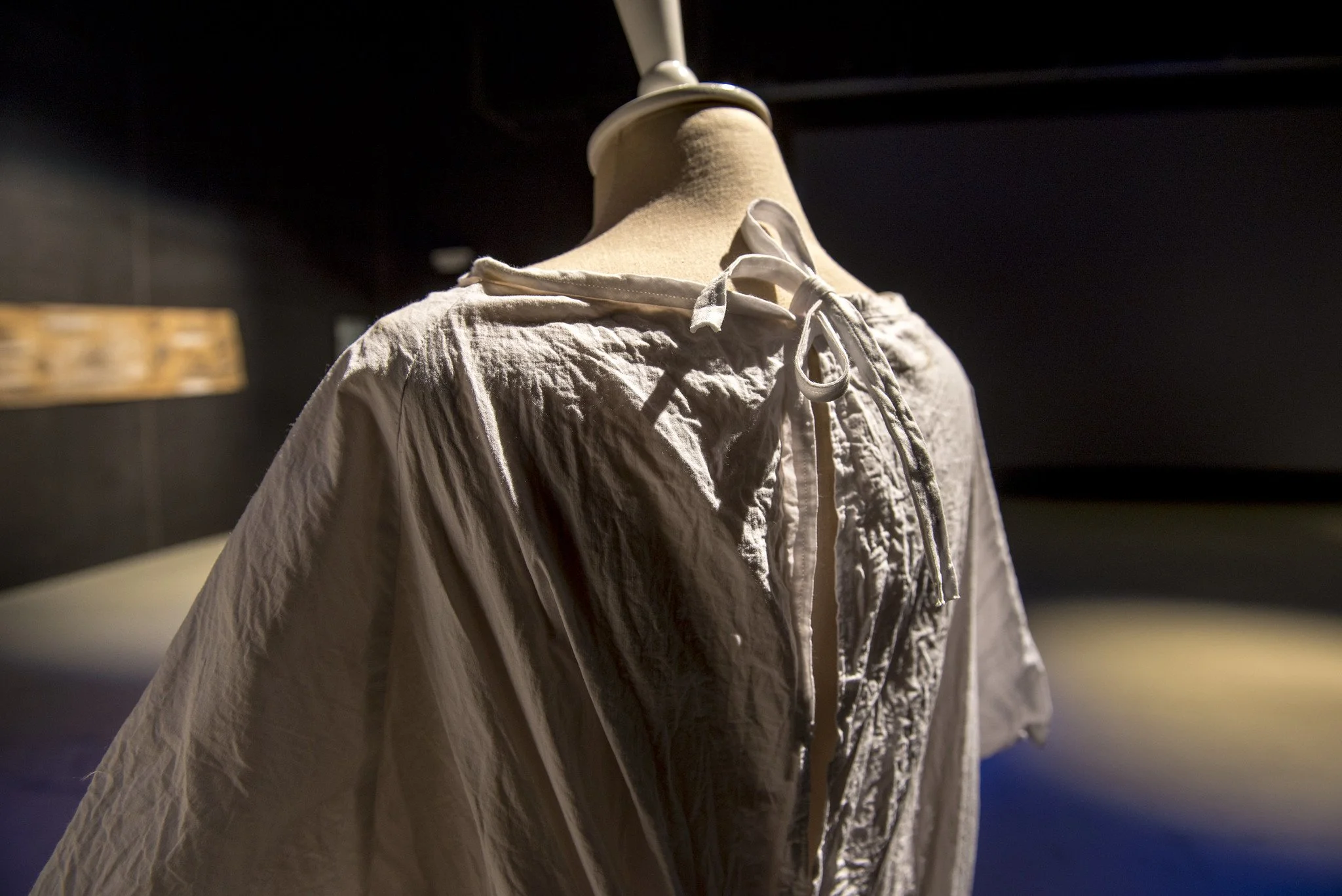 The back of a white hospital gown with fabric ties on a dress form in dramatic lighting