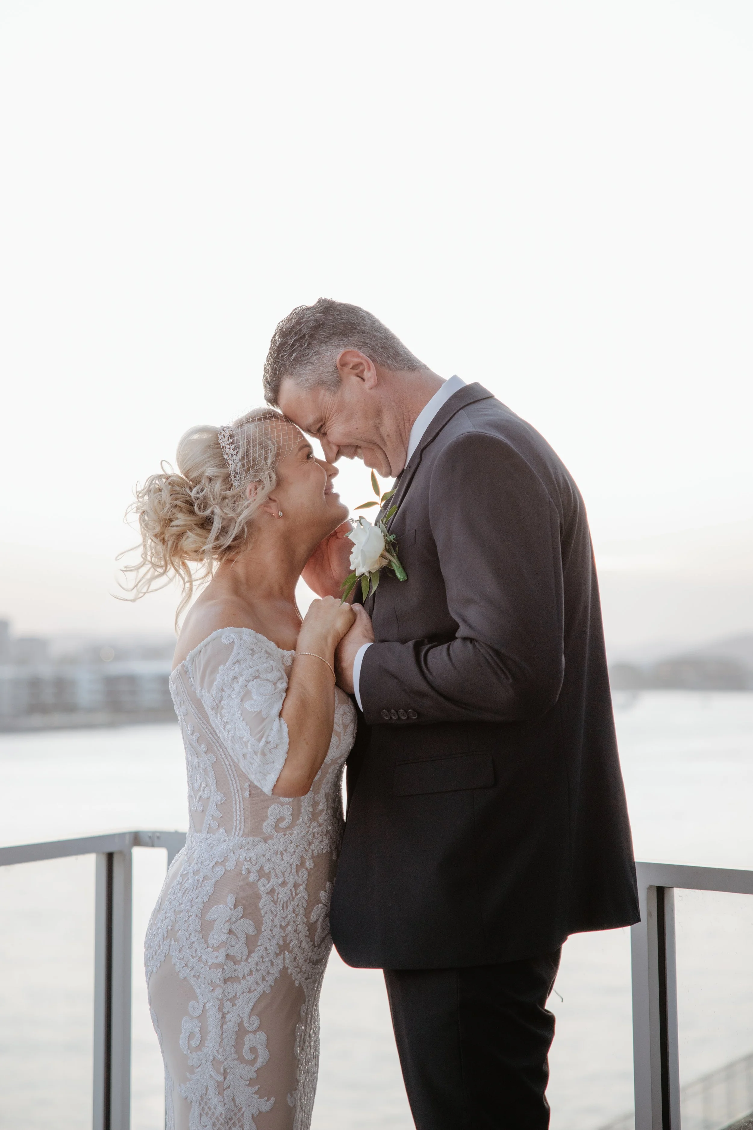 Ange and Kevin sharing a tender moment overlooking the Brisbane River at Waters Edge Weddings & Events in Hamilton.
