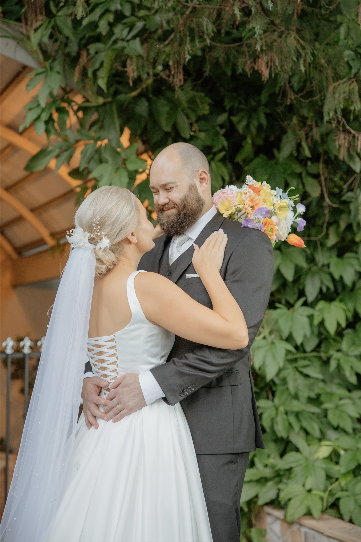 Chelsea and Del embracing beside lush greenery at their Boulevard Gardens wedding in Indooroopilly.