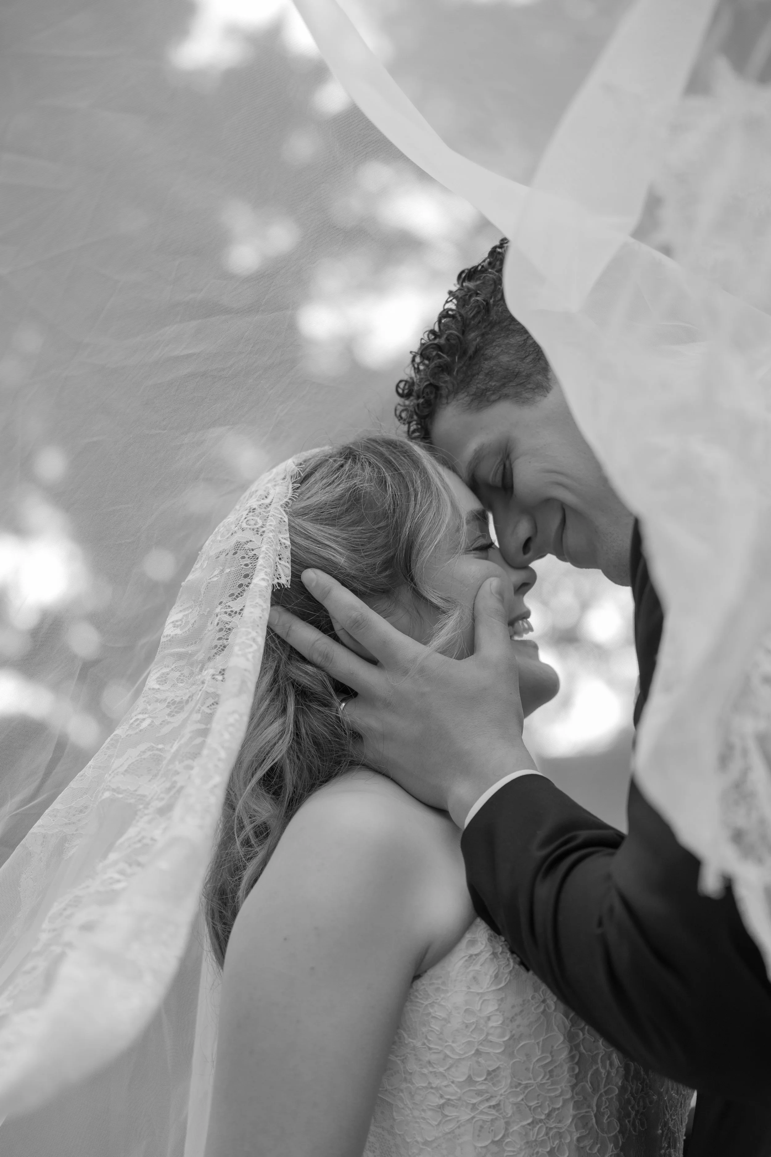 A bride and groom sharing a kiss under a wedding veil, with the bride wearing a lace dress and veil, and the groom in a suit, celebrating their wedding at Gabbinbar Homestead