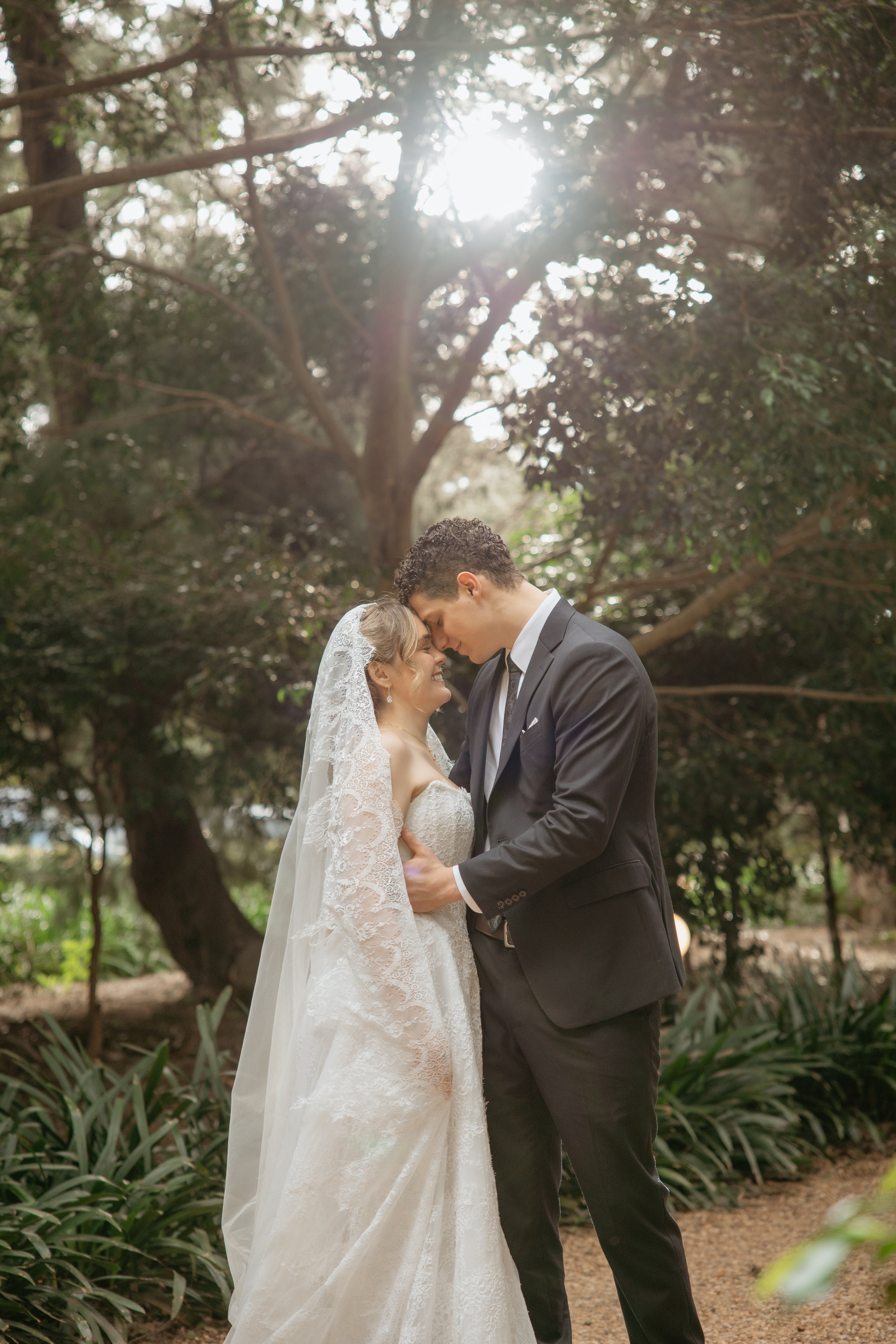 Bride and groom sharing an intimate moment beneath sunlit trees at Gabbinbar Homestead in Toowoomba.