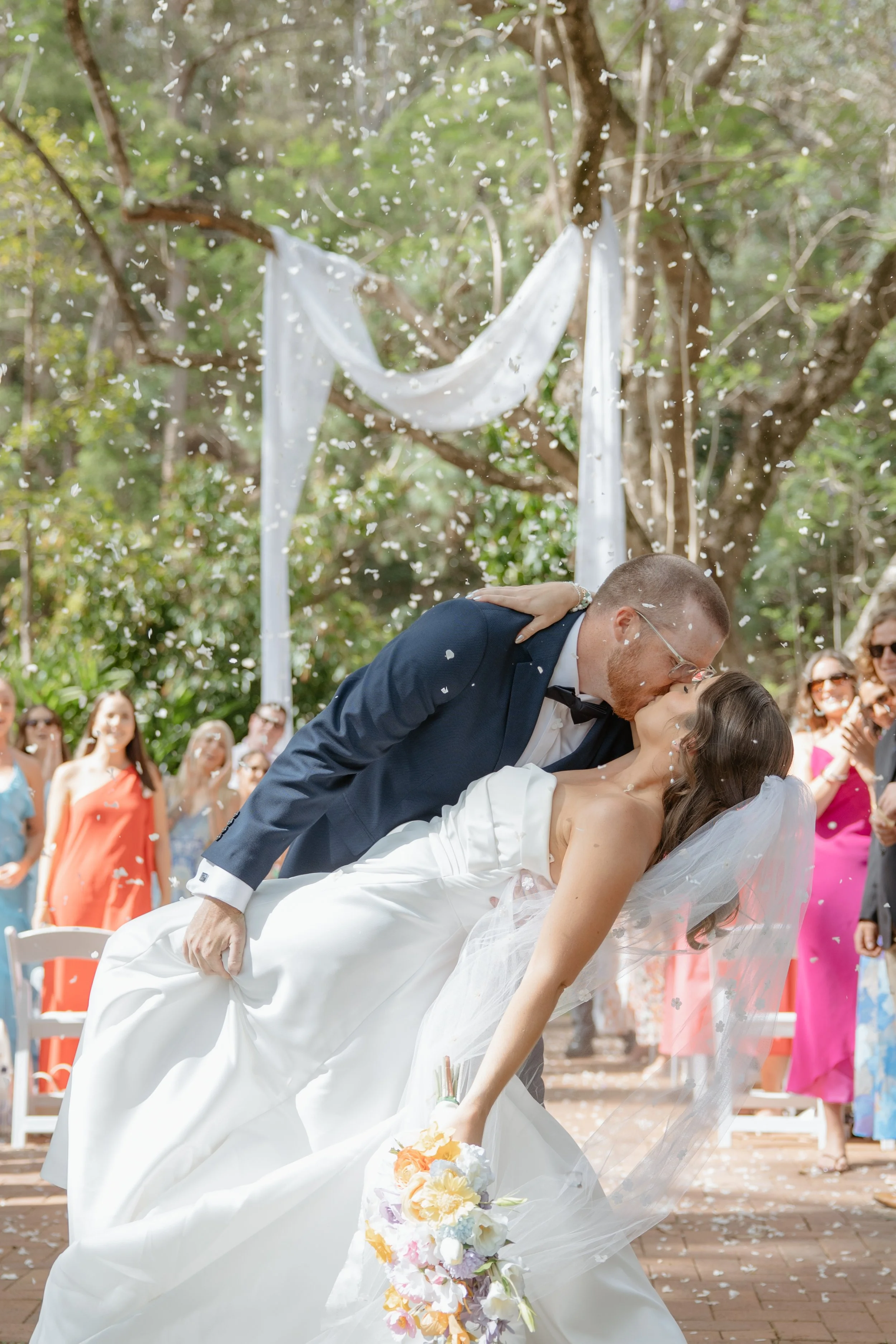 Bride and groom sharing a celebratory kiss beneath falling confetti after their outdoor wedding ceremony at Bundaleer.