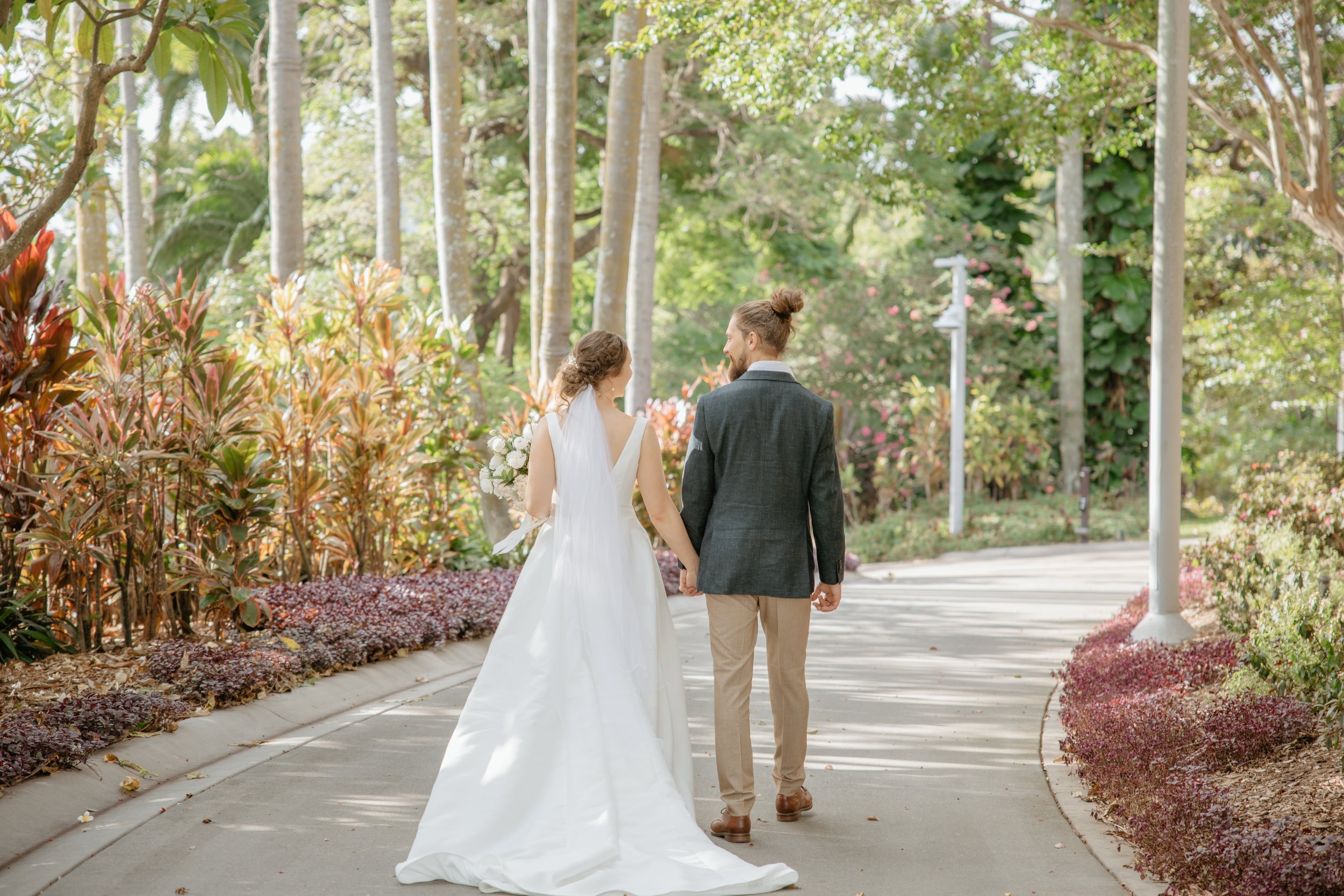 Alexa and Ryan walking hand in hand through the gardens at Roma Street Parkland in Brisbane on their wedding day.