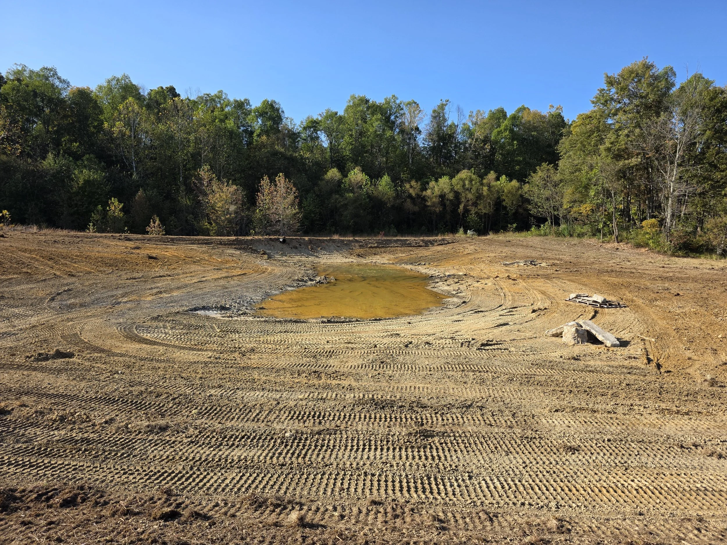 Freshly constructed pond with earthen dam and culvert overflow pipe