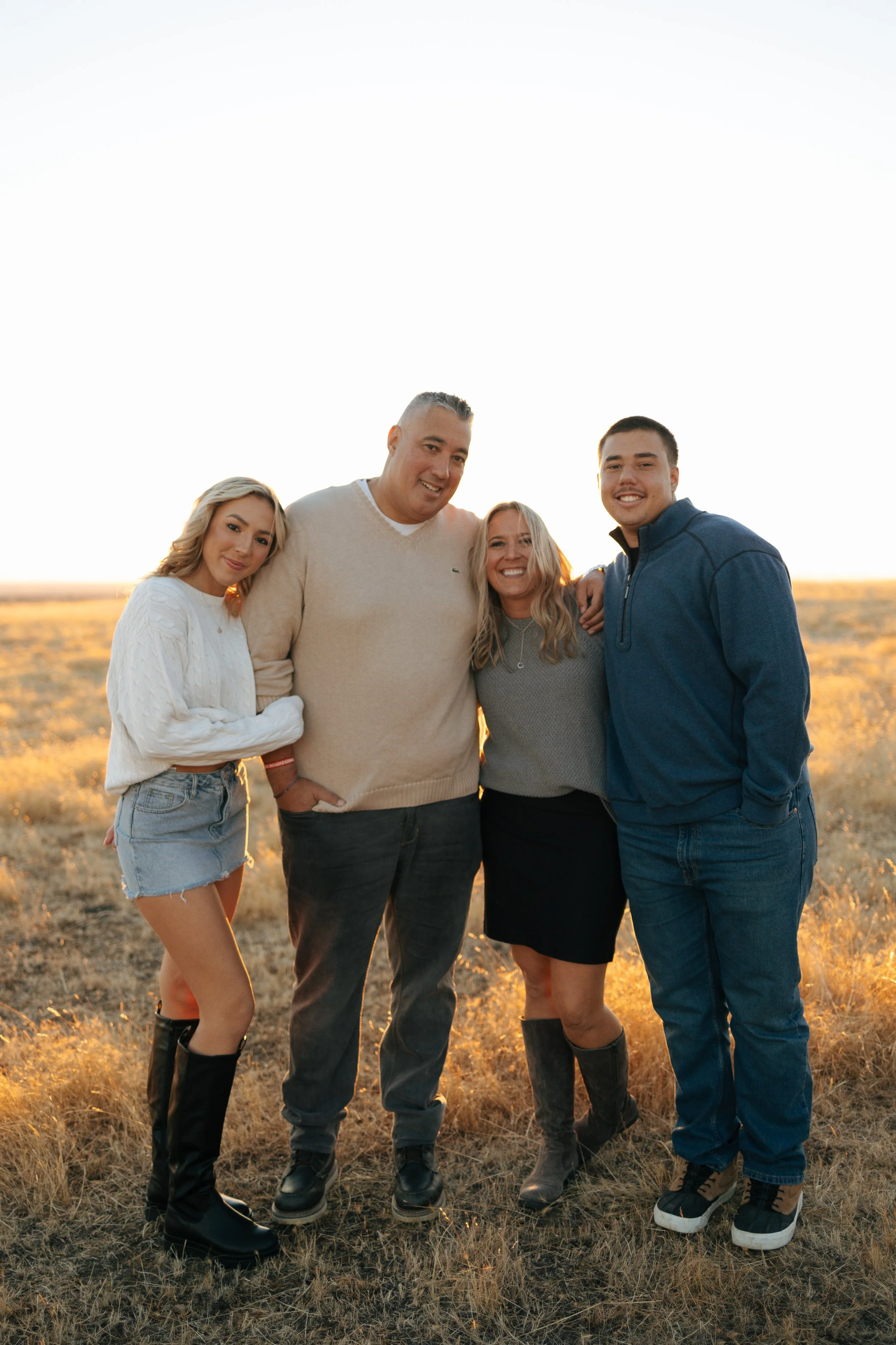 Four people standing together in a field during sunset, smiling at the camera.