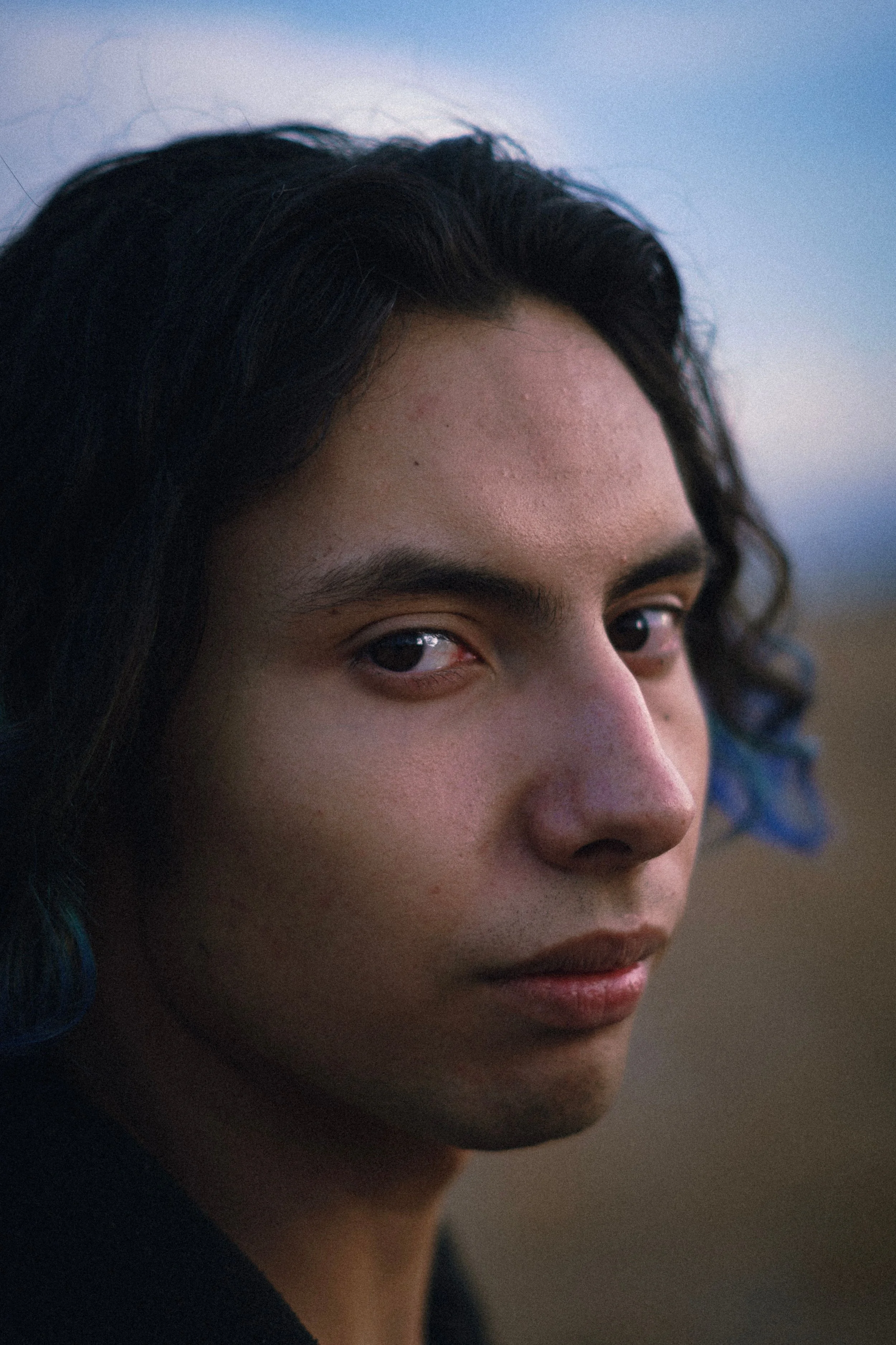Close-up of a person's face showing their right eye, nose, lips, and dark wavy hair with a hint of blue.