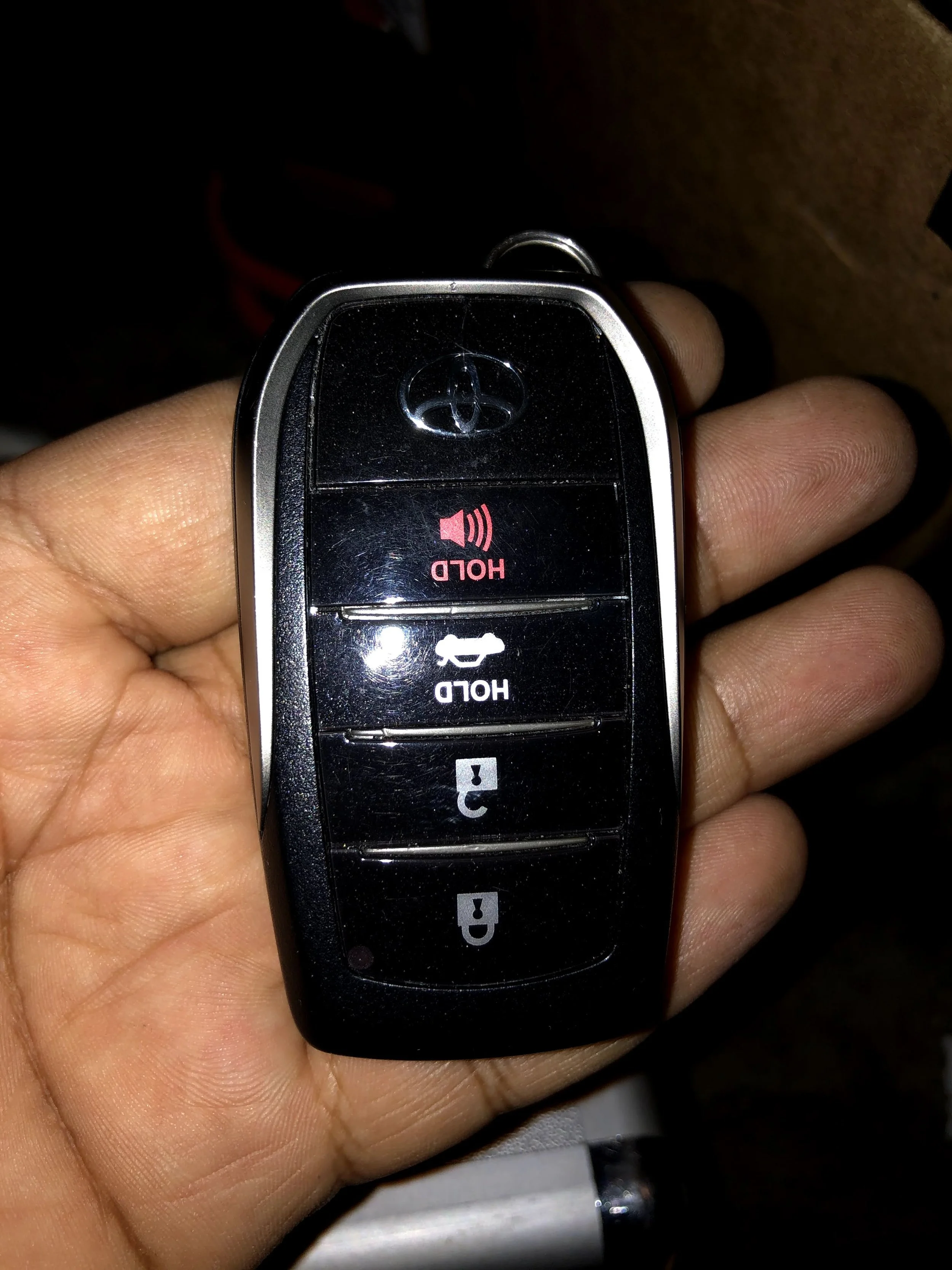 Close-up of a hand holding a Toyota car key remote with buttons for lock, unlock, trunk, and panic alarm.